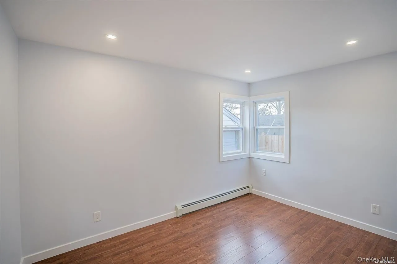 Empty room with a baseboard heating unit, dark wood-style floors, and recessed lighting Empty room with a baseboard heating unit, dark wood-style floors, and recessed lighting