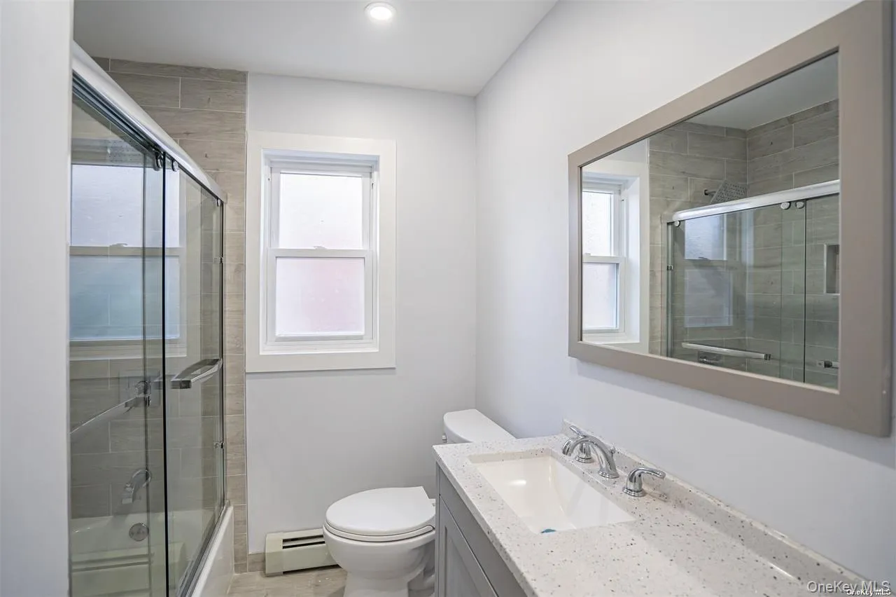 Full bath with shower / bath combination with glass door, vanity, plenty of natural light, a baseboard heating unit, and recessed lighting Full bath with shower / bath combination with glass door, vanity, plenty of natural light, a baseboard heating unit, and recessed lighting