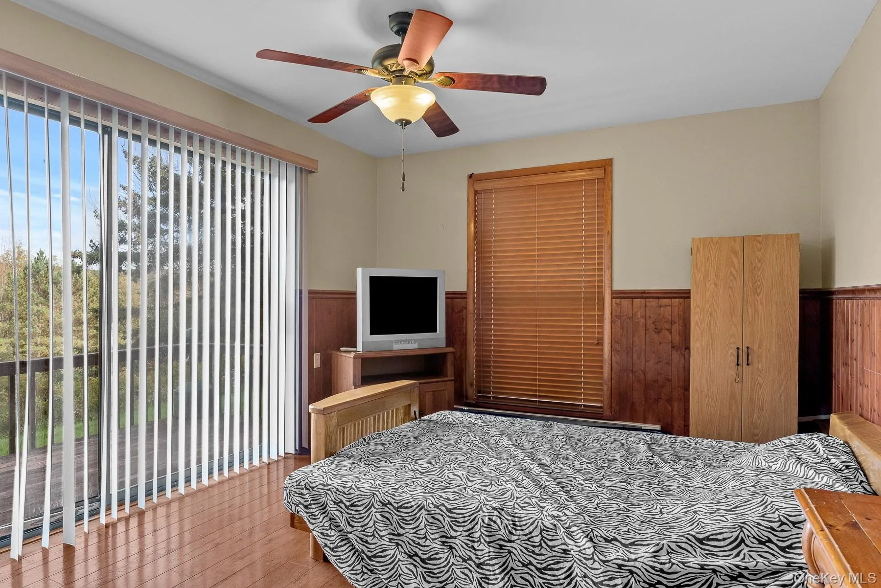 Bedroom featuring wood finished floors, wood walls, ceiling fan, access to exterior, and wainscoting Bedroom featuring wood finished floors, wood walls, ceiling fan, access to exterior, and wainscoting