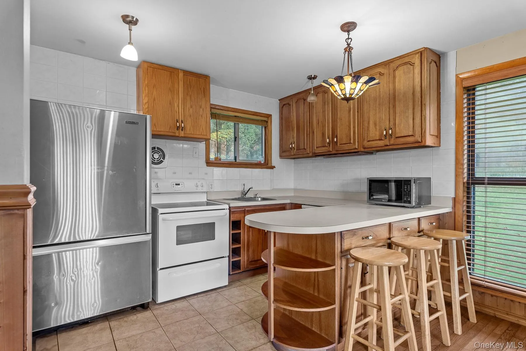 Kitchen with stainless steel appliances, decorative backsplash, a peninsula, light countertops, and brown cabinets Kitchen with stainless steel appliances, decorative backsplash, a peninsula, light countertops, and brown cabinets