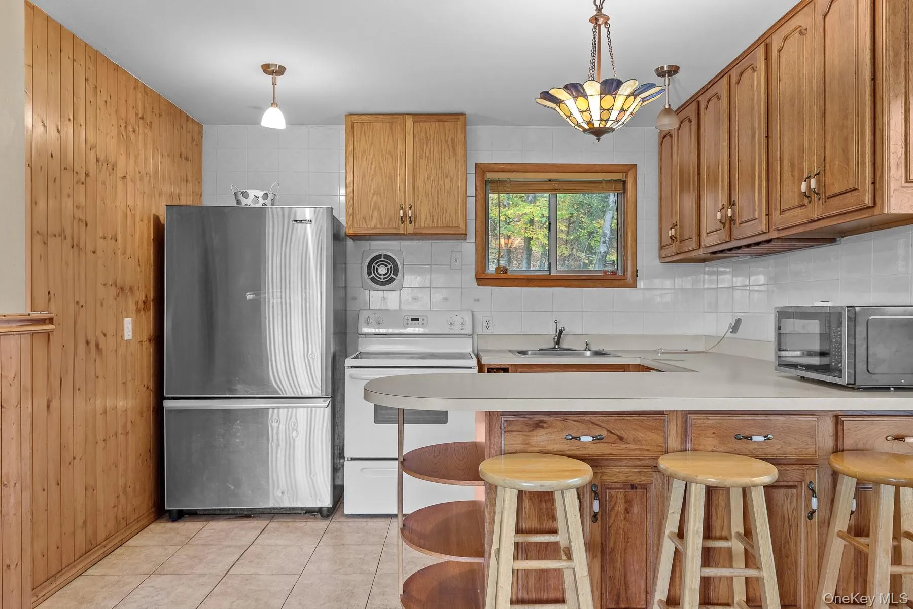 Kitchen featuring light countertops, freestanding refrigerator, white electric range, decorative backsplash, and a kitchen breakfast bar Kitchen featuring light countertops, freestanding refrigerator, white electric range, decorative backsplash, and a kitchen breakfast bar