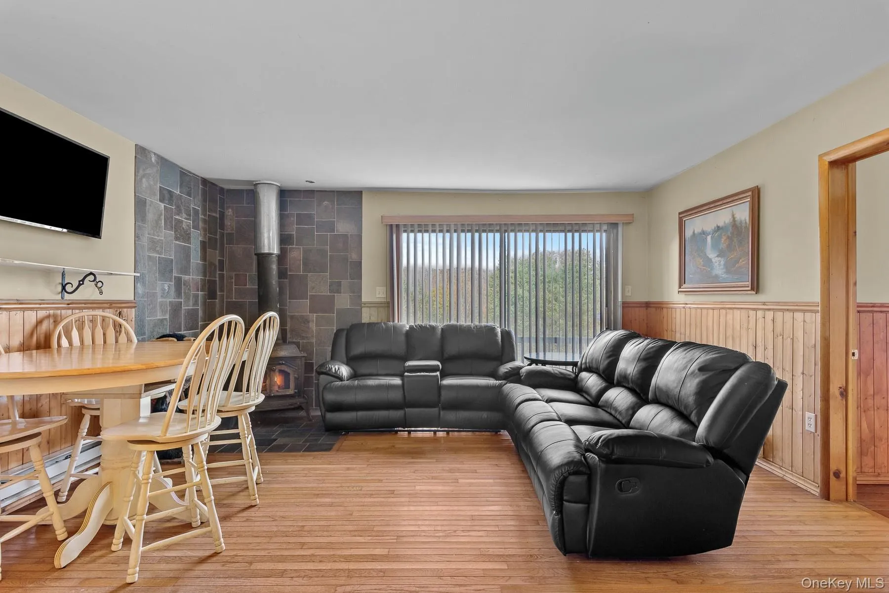 Living area featuring a wood stove, light wood-type flooring, wood walls, and wainscoting Living area featuring a wood stove, light wood-type flooring, wood walls, and wainscoting