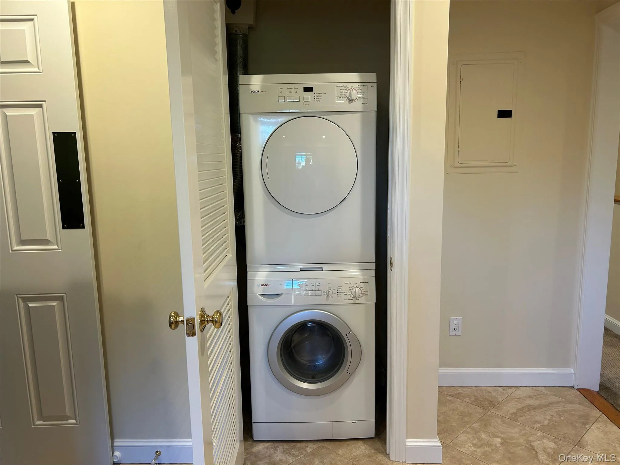 Laundry room with electric panel, stacked washer / drying machine, and light tile patterned floors Laundry room with electric panel, stacked washer / drying machine, and light tile patterned floors