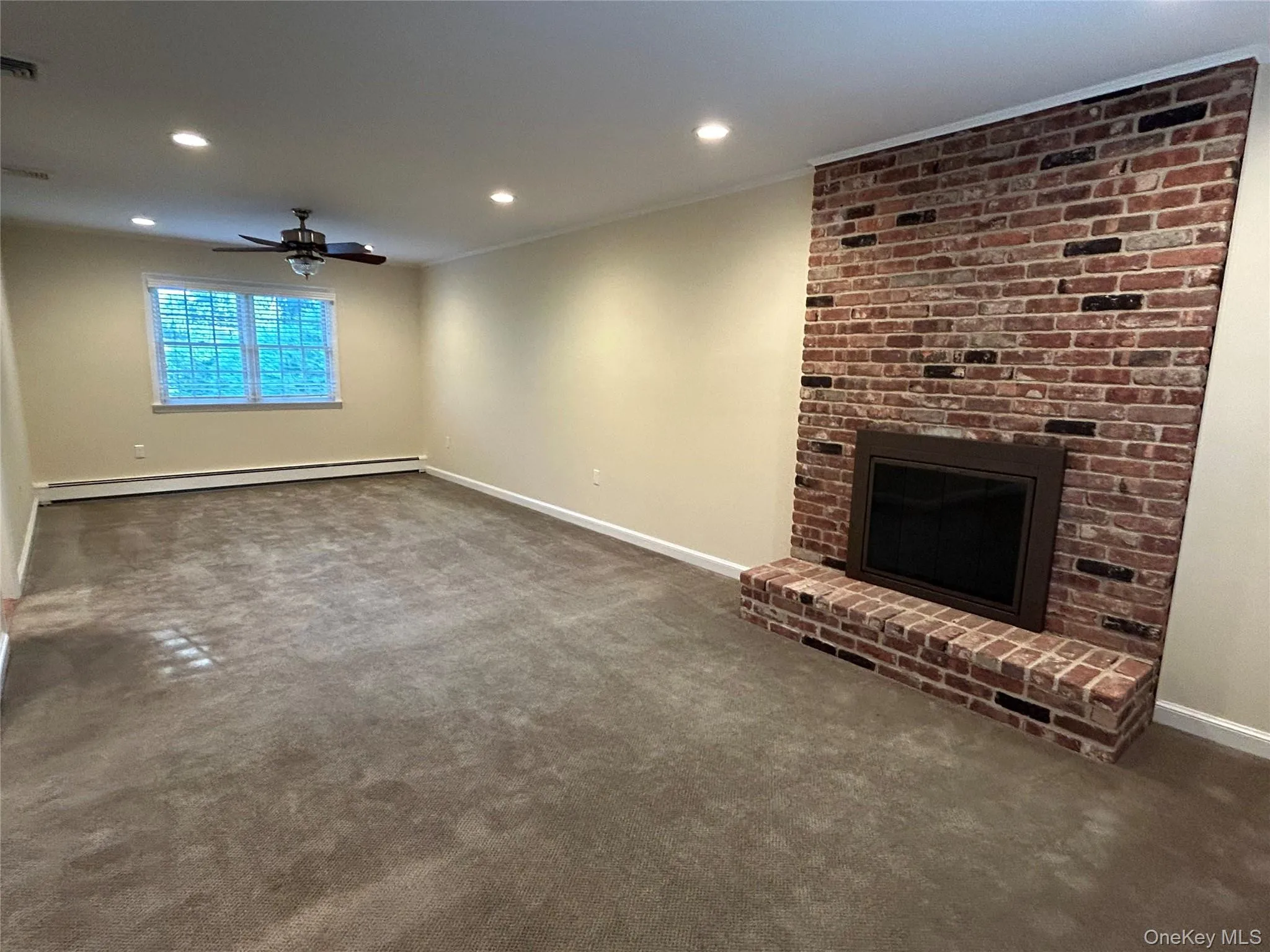 Unfurnished living room with dark colored carpet, recessed lighting, a brick fireplace, a baseboard radiator, and a ceiling fan Unfurnished living room with dark colored carpet, recessed lighting, a brick fireplace, a baseboard radiator, and a ceiling fan
