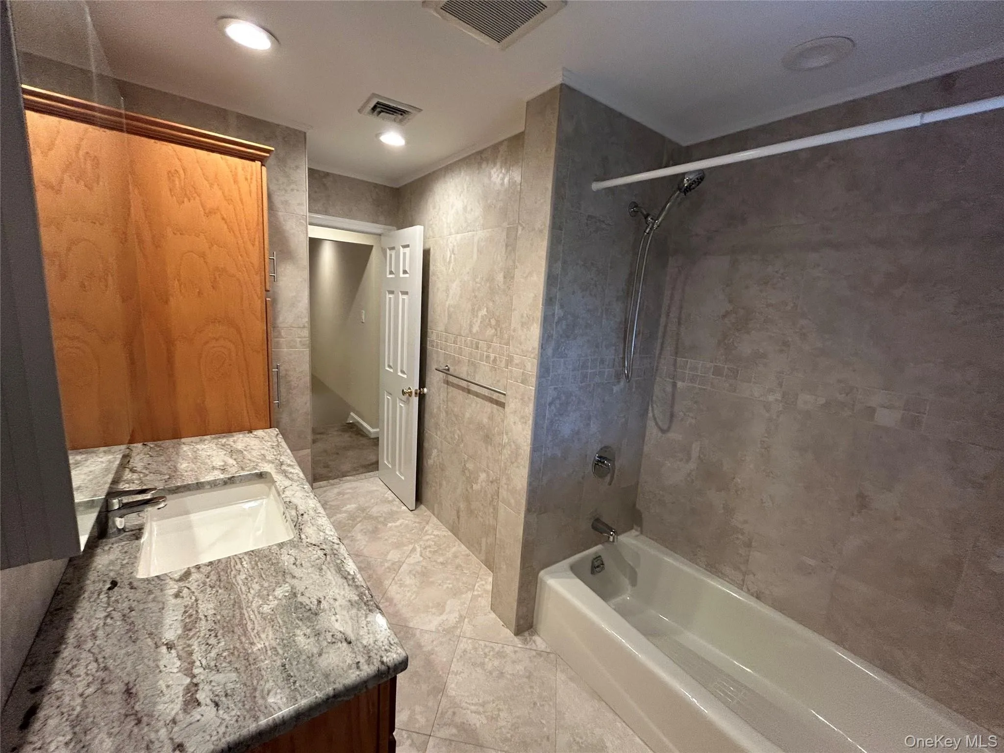 Bathroom with washtub / shower combination, tile walls, double vanity, recessed lighting, and light tile patterned flooring Bathroom with washtub / shower combination, tile walls, double vanity, recessed lighting, and light tile patterned flooring