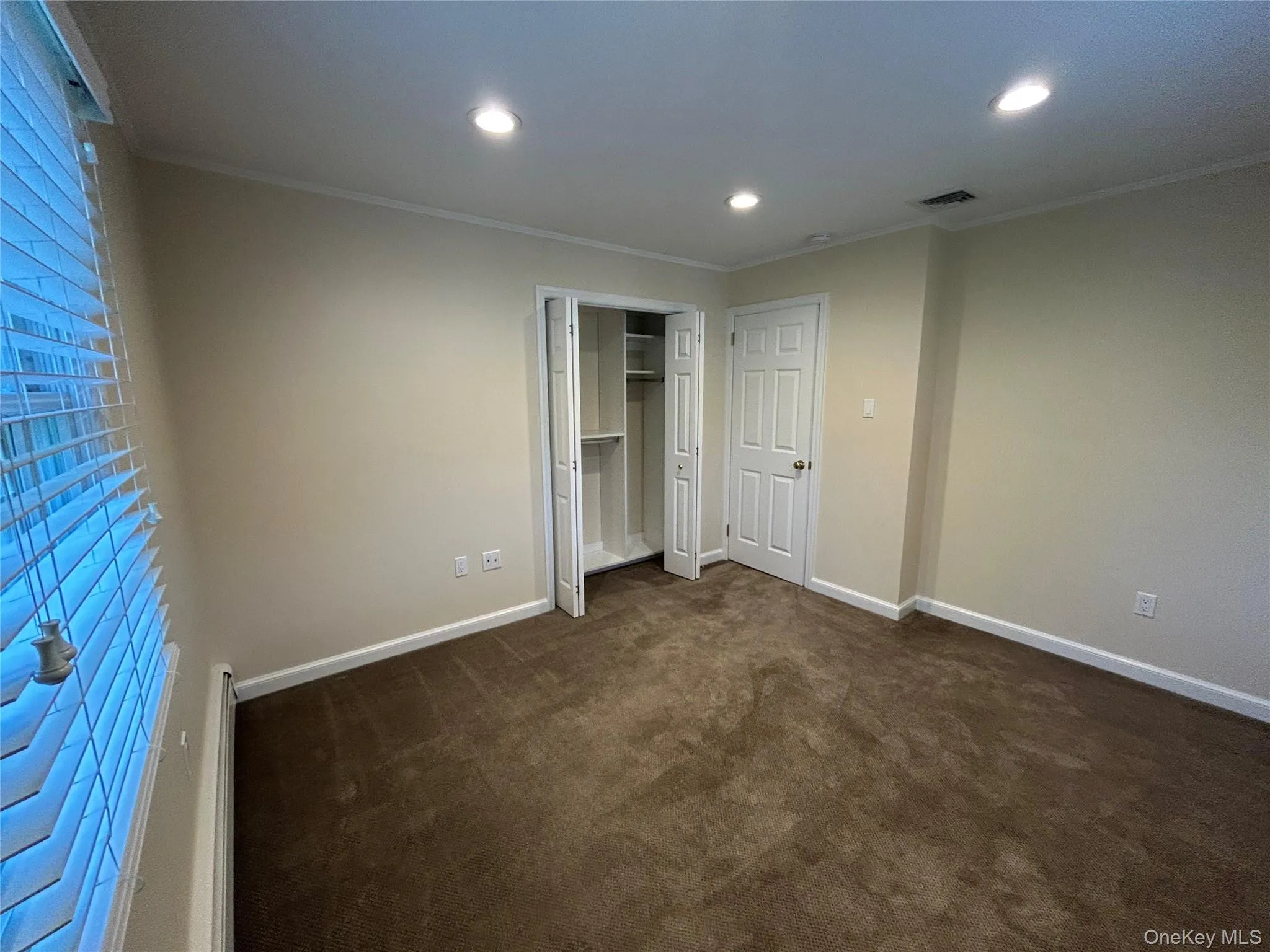 Unfurnished bedroom with dark carpet, crown molding, a closet, recessed lighting, and baseboard heating Unfurnished bedroom with dark carpet, crown molding, a closet, recessed lighting, and baseboard heating
