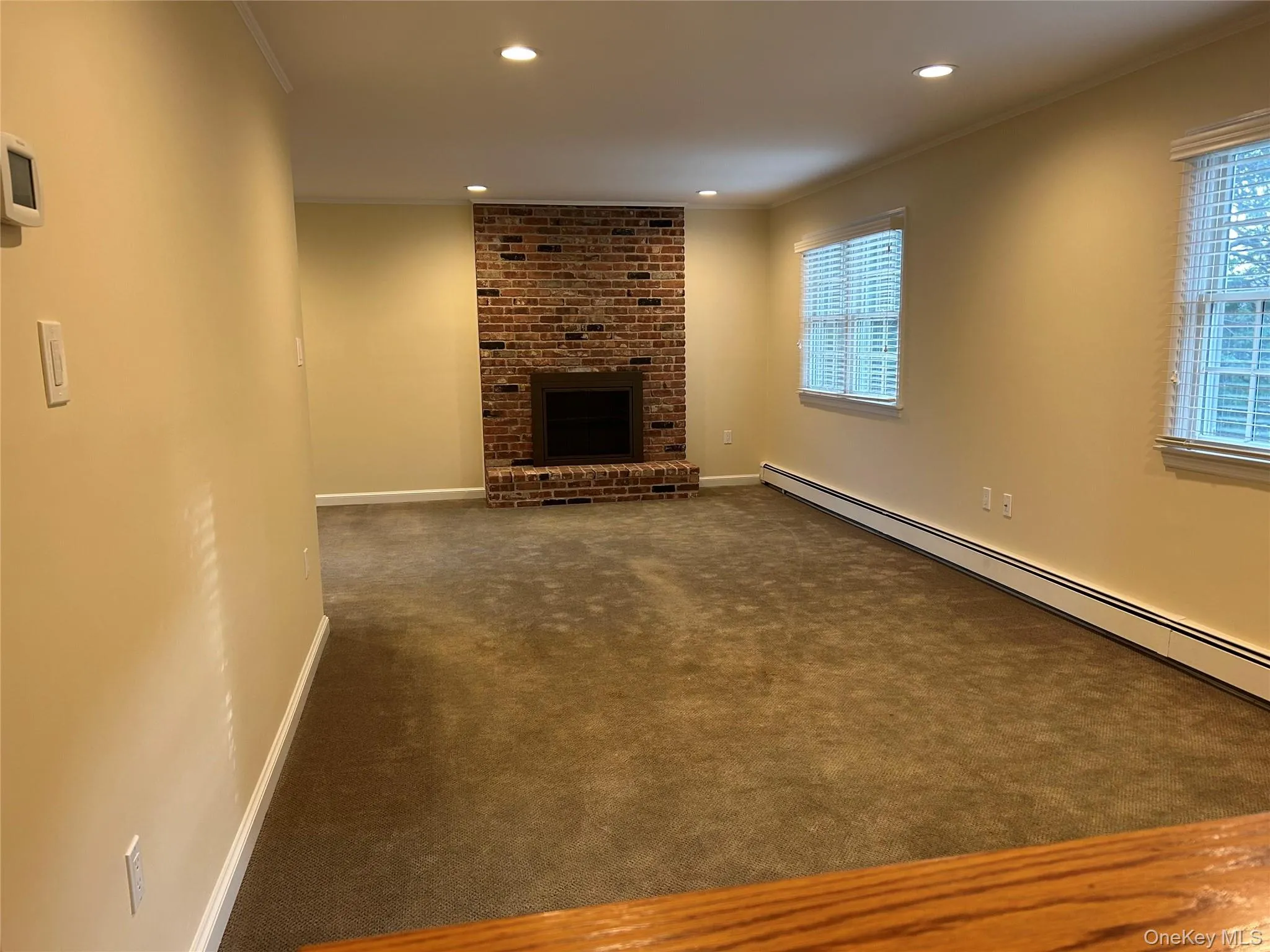 Unfurnished living room featuring a brick fireplace, crown molding, dark carpet, a baseboard heating unit, and recessed lighting Unfurnished living room featuring a brick fireplace, crown molding, dark carpet, a baseboard heating unit, and recessed lighting