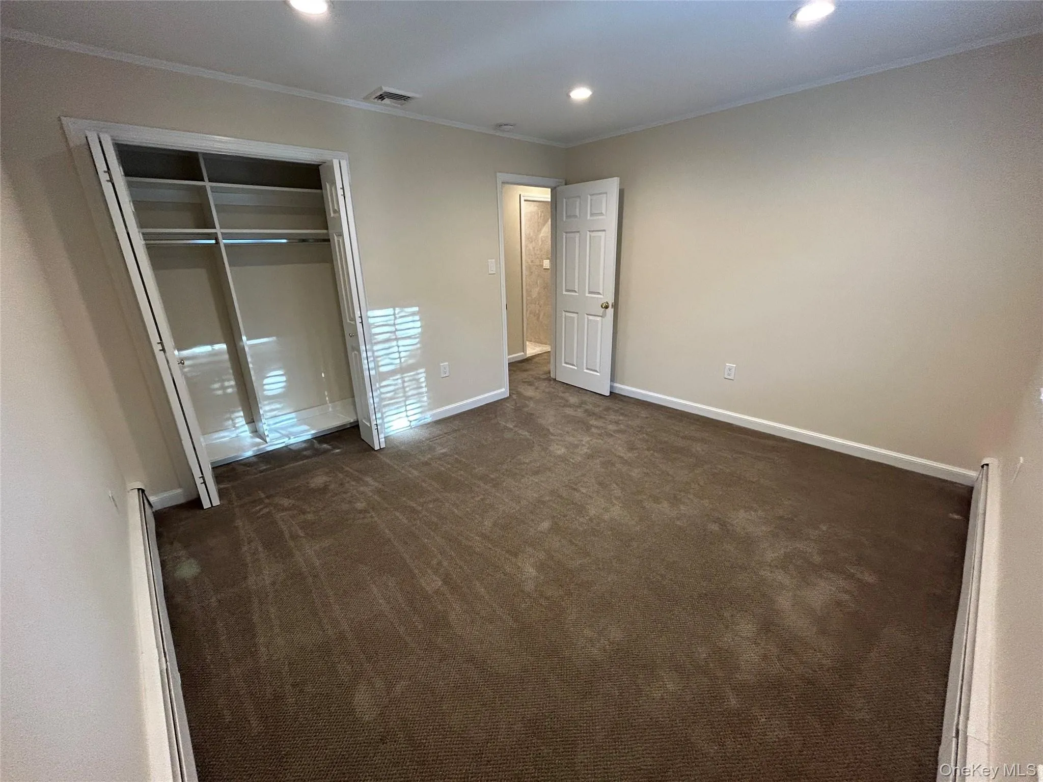 Unfurnished bedroom with crown molding, dark carpet, recessed lighting, baseboard heating, and a closet Unfurnished bedroom with crown molding, dark carpet, recessed lighting, baseboard heating, and a closet