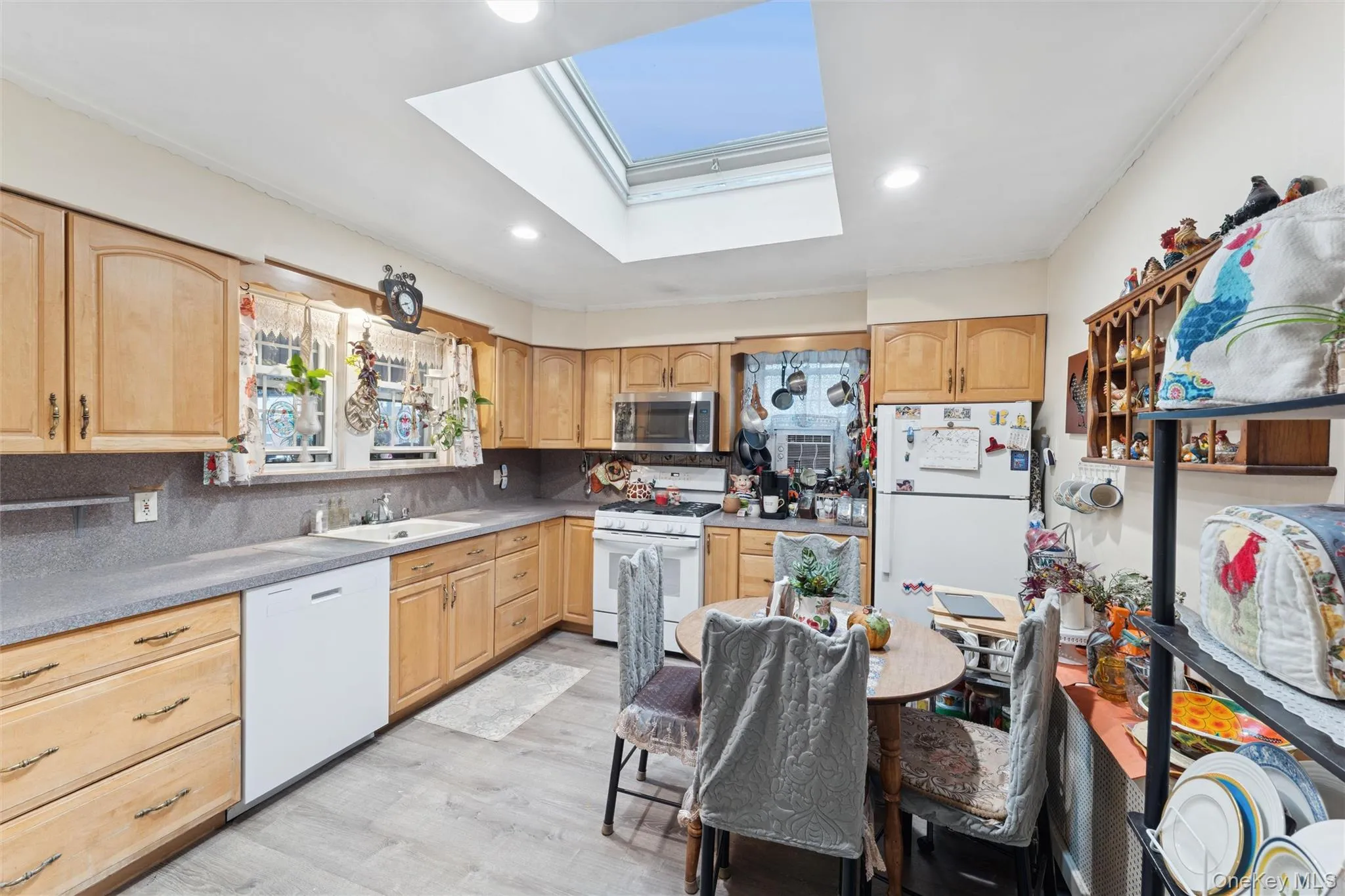 Kitchen featuring a skylight, white appliances, light wood-style floors, backsplash, and recessed lighting Kitchen featuring a skylight, white appliances, light wood-style floors, backsplash, and recessed lighting