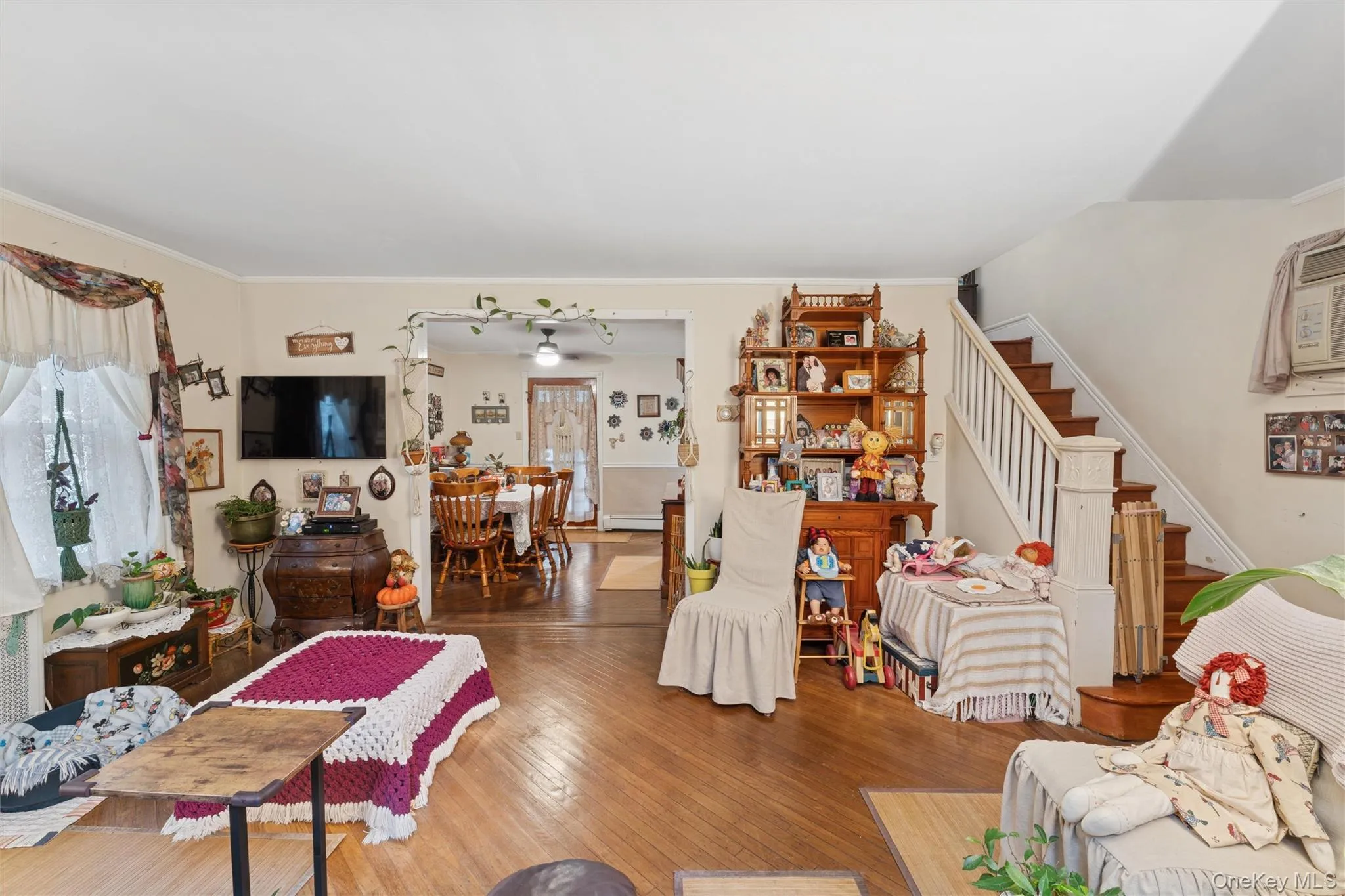 Living area with wood finished floors, stairway, ornamental molding, and a baseboard heating unit Living area with wood finished floors, stairway, ornamental molding, and a baseboard heating unit
