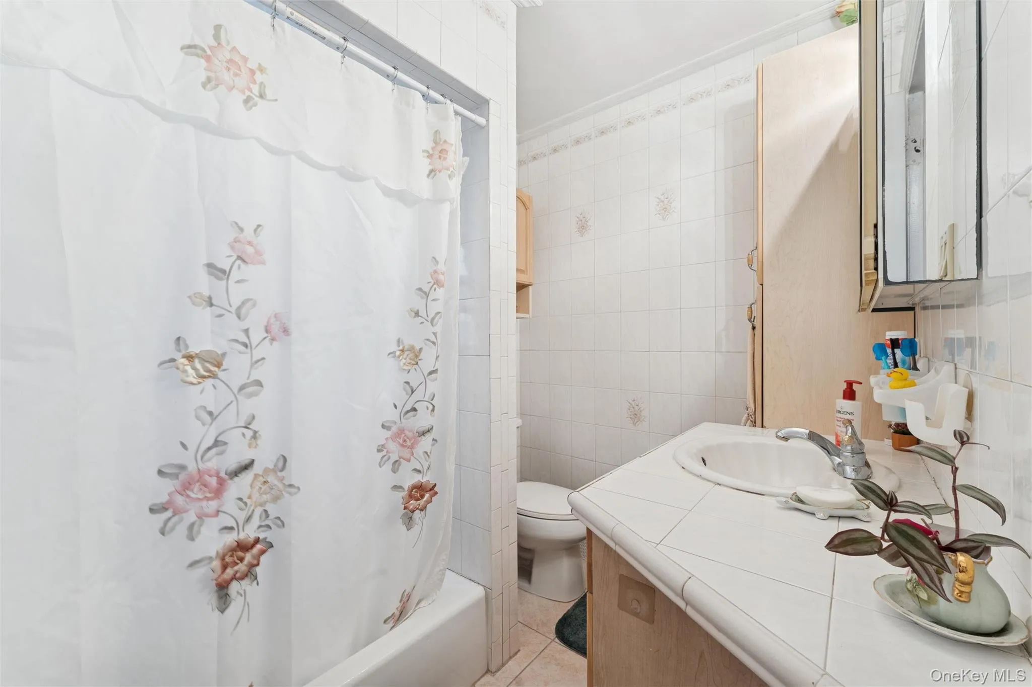 Bathroom featuring tile walls, shower / bathtub combination with curtain, vanity, and light tile patterned floors Bathroom featuring tile walls, shower / bathtub combination with curtain, vanity, and light tile patterned floors