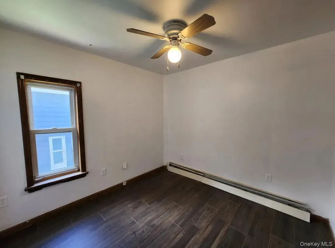 Spare room with a baseboard heating unit, dark wood-type flooring, and a ceiling fan Spare room with a baseboard heating unit, dark wood-type flooring, and a ceiling fan