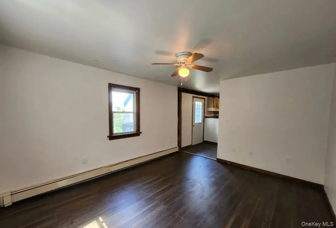Empty room with a baseboard heating unit, dark wood-style flooring, and a ceiling fan Empty room with a baseboard heating unit, dark wood-style flooring, and a ceiling fan