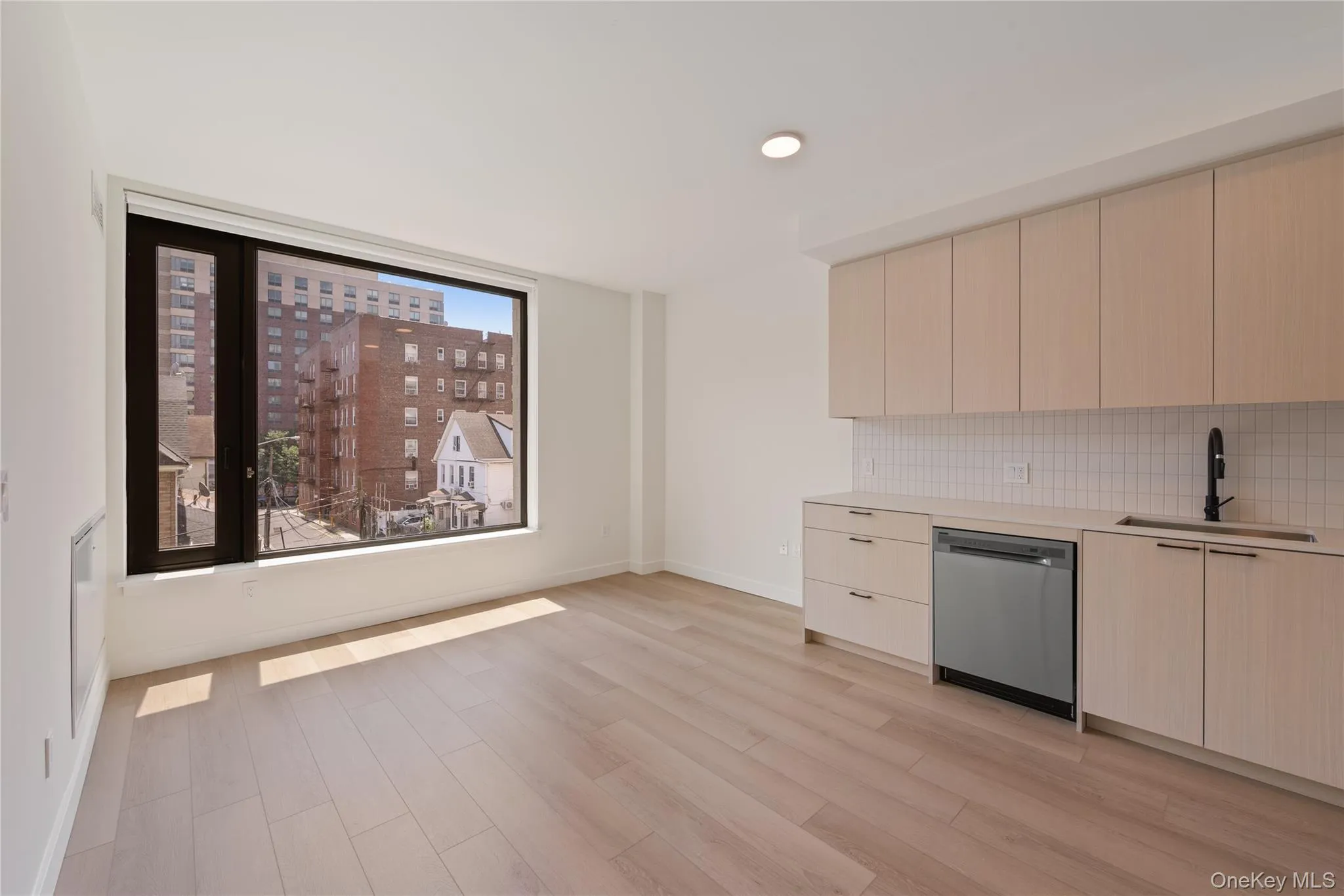 Kitchen with modern cabinets, stainless steel dishwasher, light brown cabinetry, backsplash, and light wood-style flooring Kitchen with modern cabinets, stainless steel dishwasher, light brown cabinetry, backsplash, and light wood-style flooring