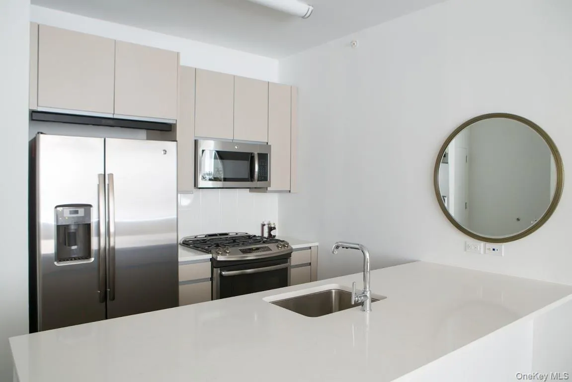 Kitchen featuring appliances with stainless steel finishes, light countertops, tasteful backsplash, gray cabinetry, and a peninsula Kitchen featuring appliances with stainless steel finishes, light countertops, tasteful backsplash, gray cabinetry, and a peninsula