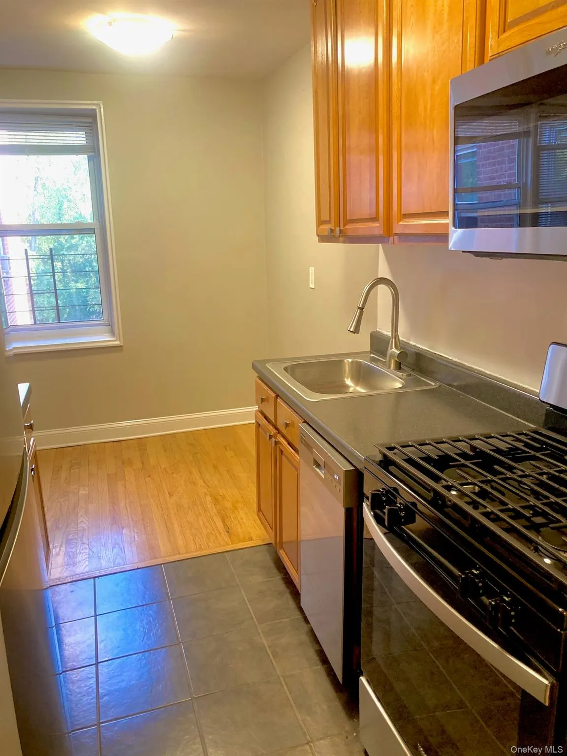 Kitchen featuring appliances with stainless steel finishes, brown cabinetry, dark tile patterned flooring, and dark countertops Kitchen featuring appliances with stainless steel finishes, brown cabinetry, dark tile patterned flooring, and dark countertops