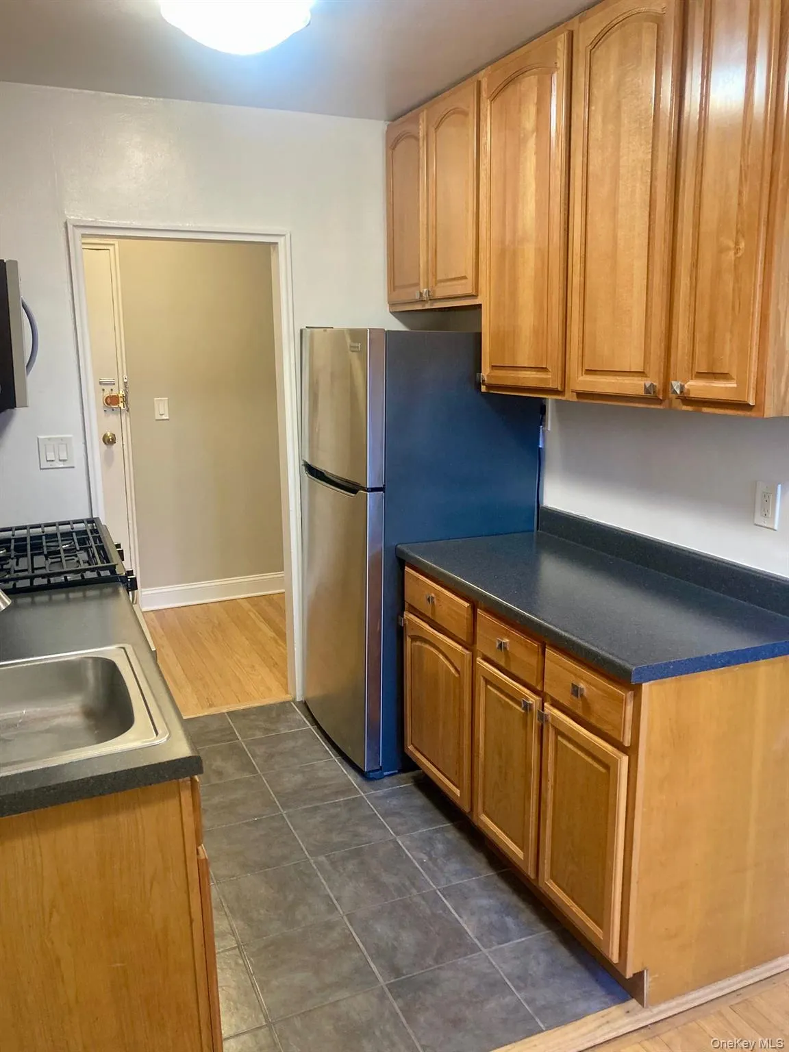 Kitchen with dark countertops, stainless steel appliances, dark tile patterned floors, and brown cabinets Kitchen with dark countertops, stainless steel appliances, dark tile patterned floors, and brown cabinets