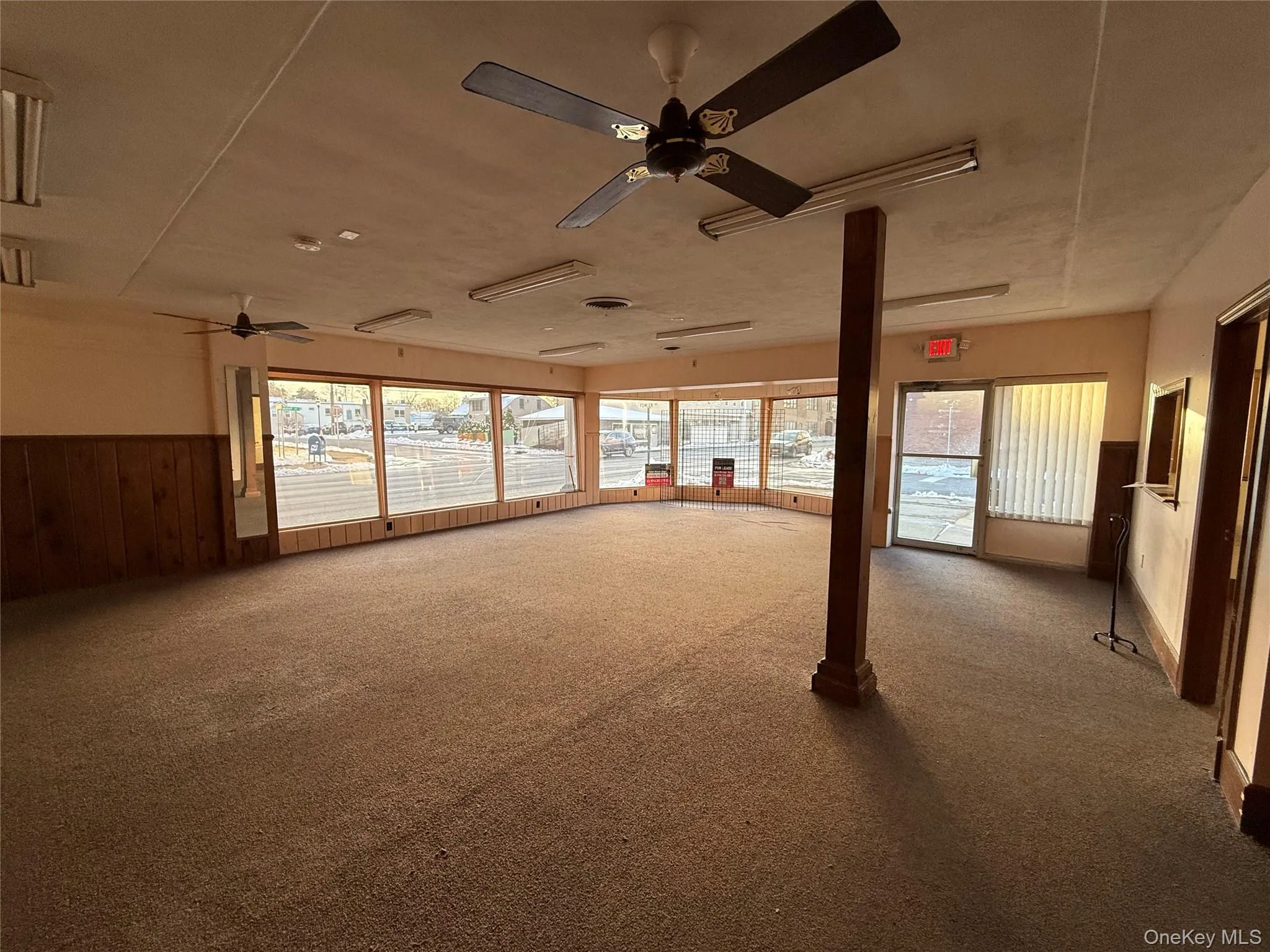 Unfurnished Retail room featuring wooden walls, wainscoting, healthy amount of natural light, carpet floors, and a ceiling fan Unfurnished Retail room featuring wooden walls, wainscoting, healthy amount of natural light, carpet floors, and a ceiling fan