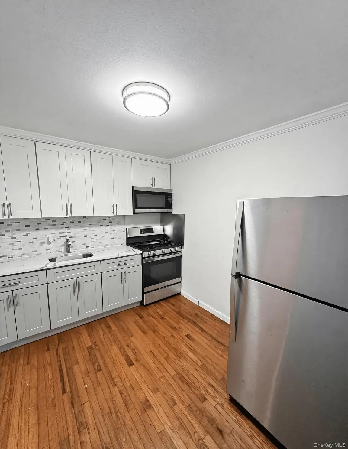 Kitchen featuring stainless steel appliances, light wood-style floors, white cabinetry, backsplash, and crown molding Kitchen featuring stainless steel appliances, light wood-style floors, white cabinetry, backsplash, and crown molding