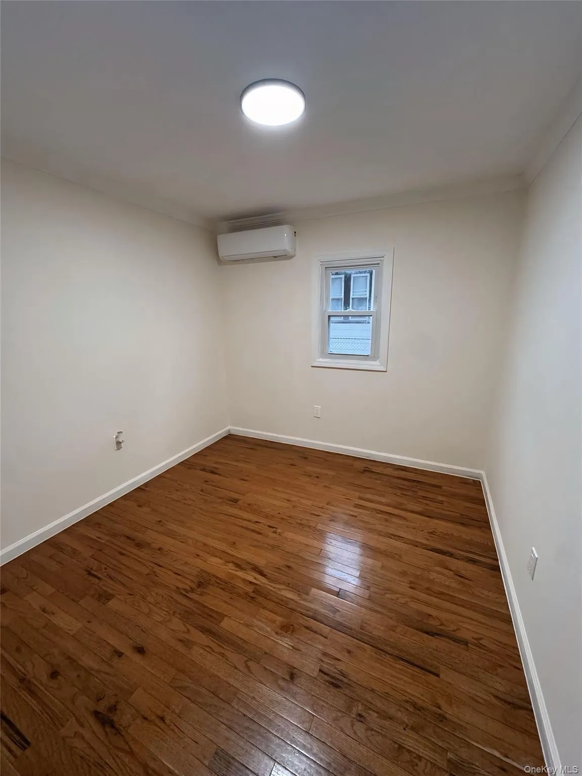 Empty room featuring dark wood finished floors, an AC wall unit, and crown molding Empty room featuring dark wood finished floors, an AC wall unit, and crown molding