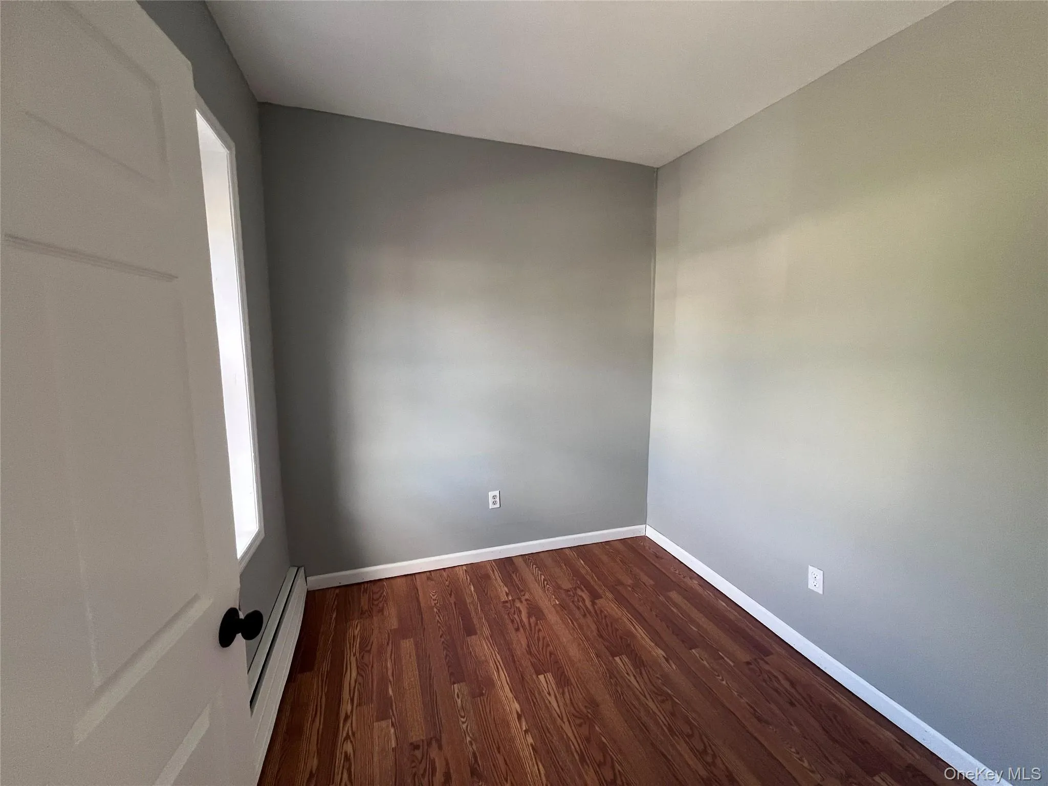 Spare room with dark wood-style flooring and a baseboard radiator Spare room with dark wood-style flooring and a baseboard radiator