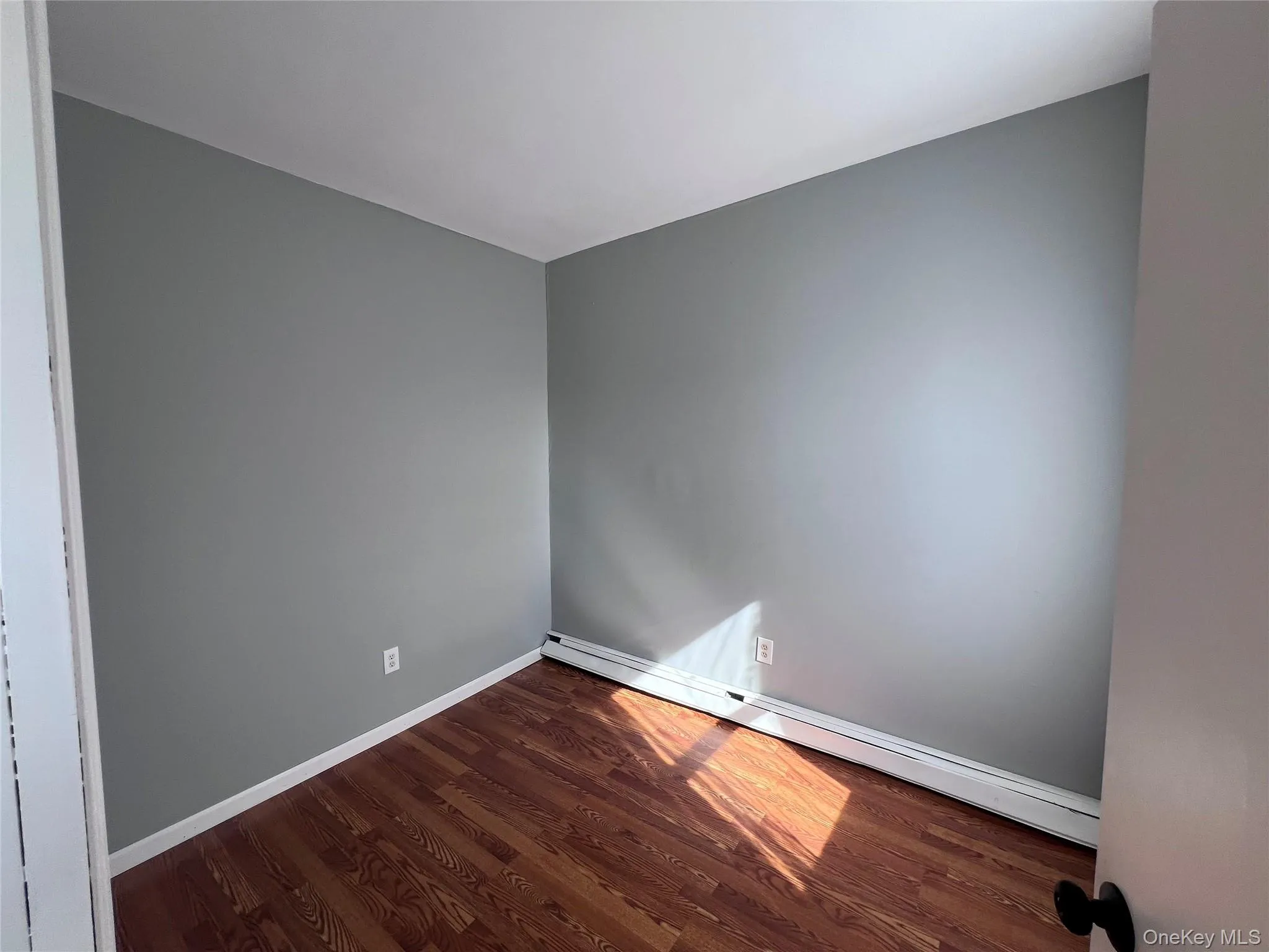 Empty room with a baseboard radiator and dark wood-style flooring Empty room with a baseboard radiator and dark wood-style flooring
