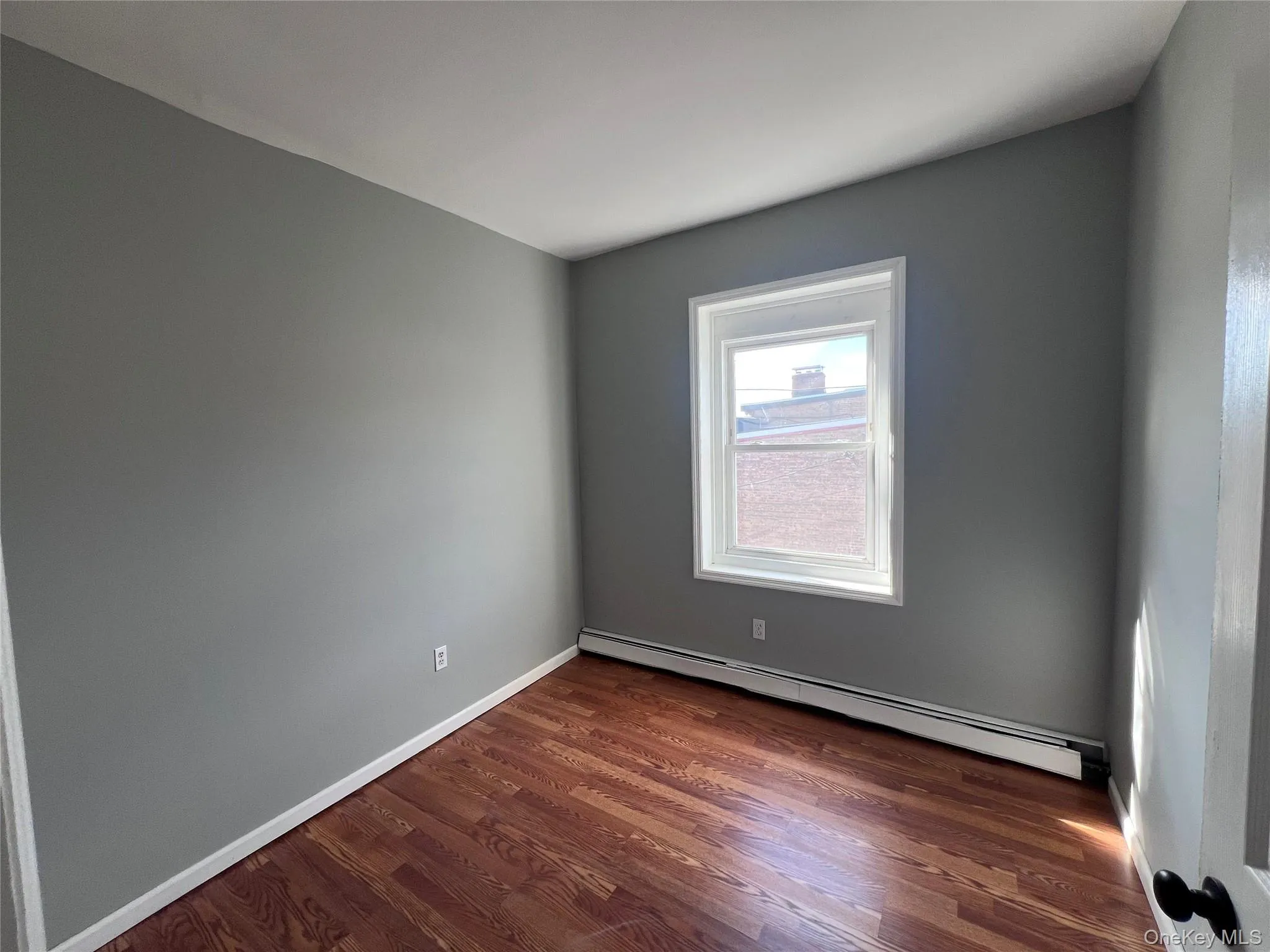 Spare room featuring baseboard heating and dark wood finished floors Spare room featuring baseboard heating and dark wood finished floors