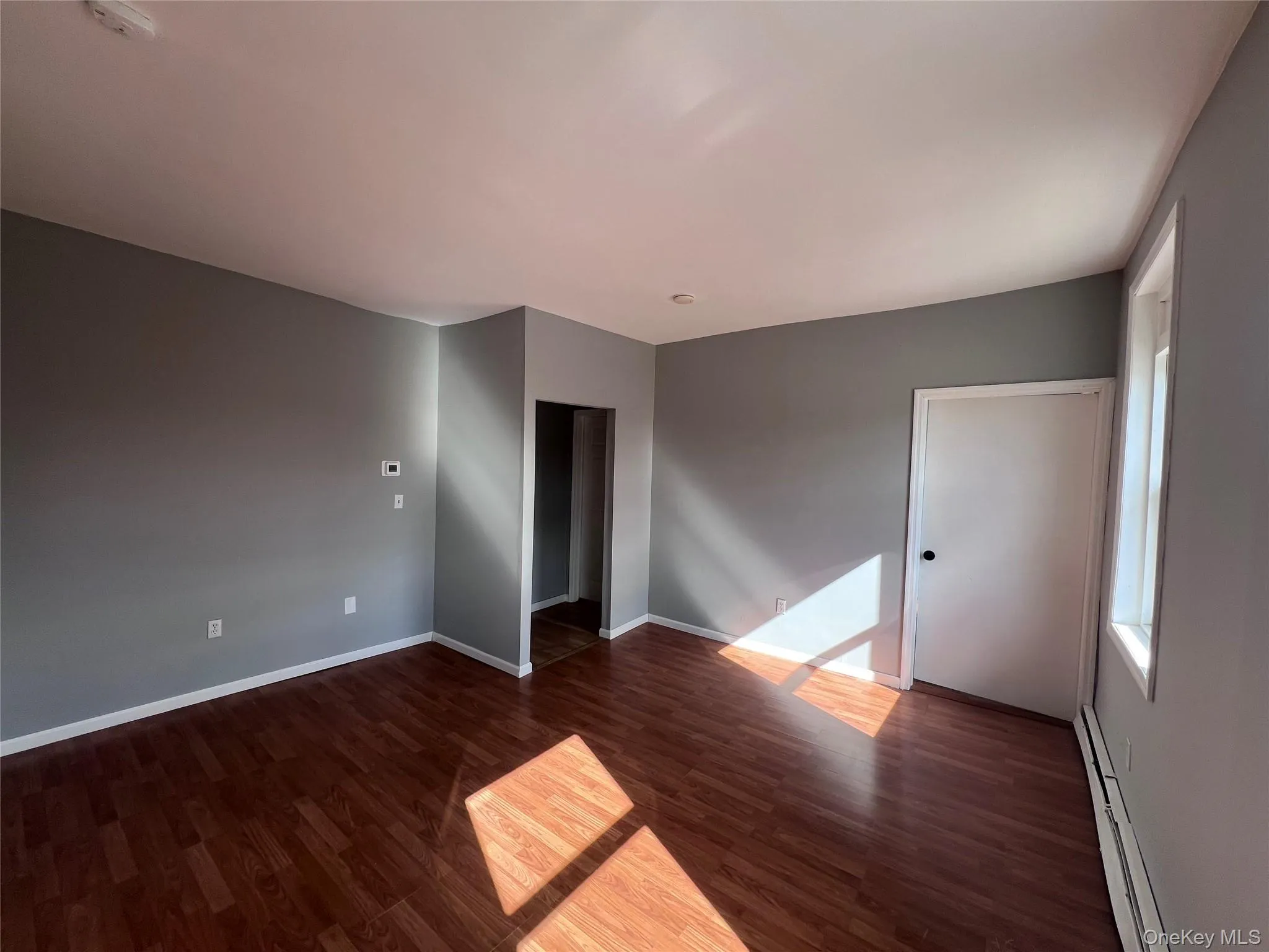 Unfurnished room with a baseboard heating unit and dark wood-type flooring Unfurnished room with a baseboard heating unit and dark wood-type flooring