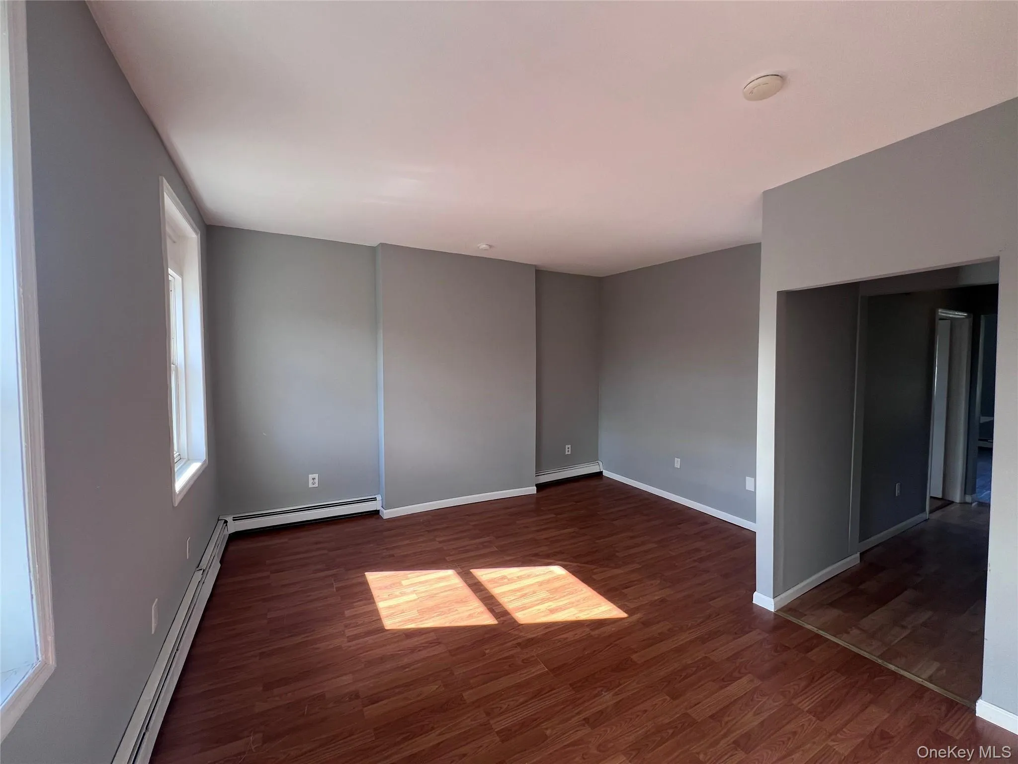 Unfurnished room with dark wood-style flooring and a baseboard heating unit Unfurnished room with dark wood-style flooring and a baseboard heating unit