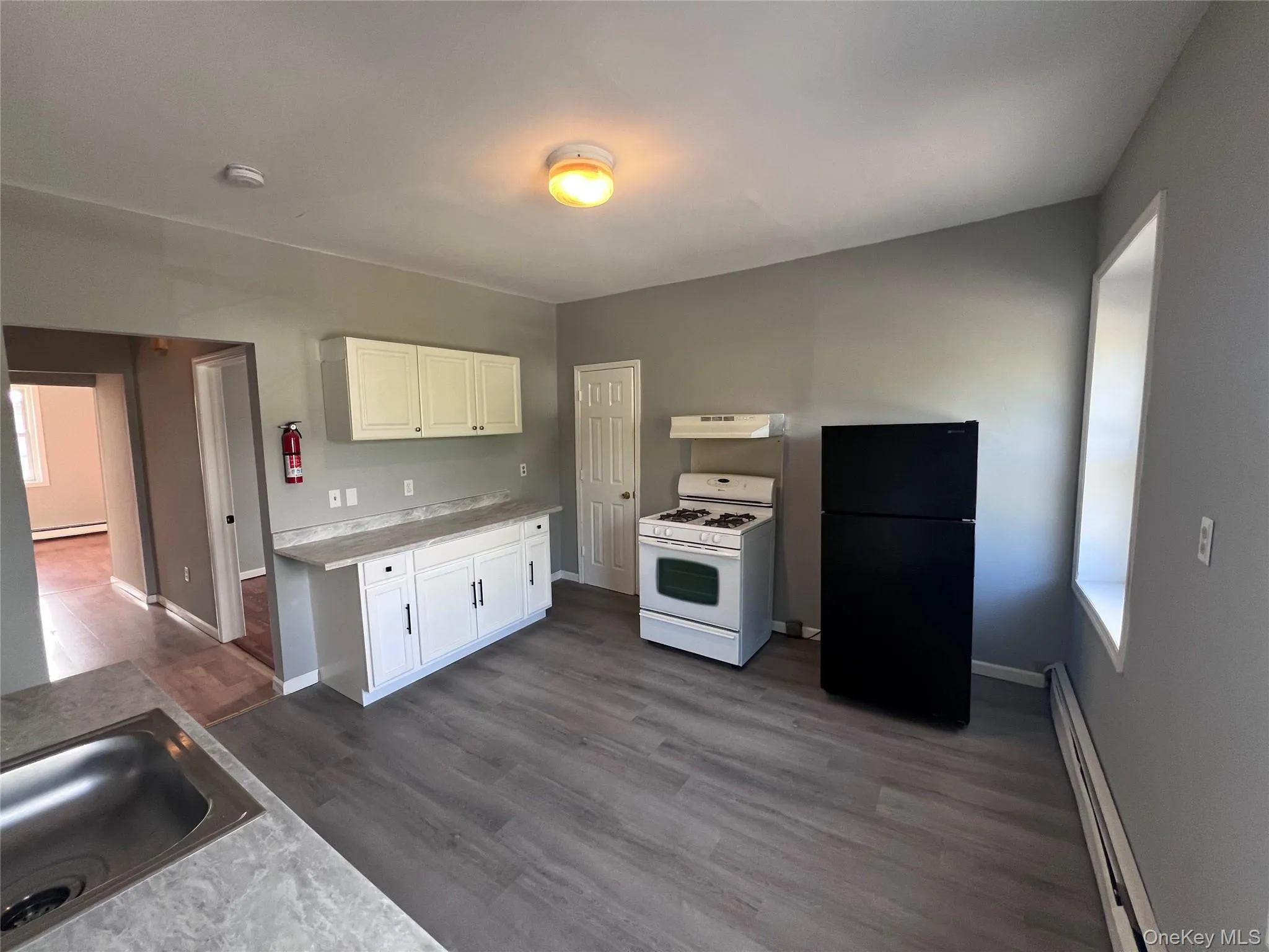 Kitchen with freestanding refrigerator, a baseboard heating unit, white range with gas stovetop, dark wood-style floors, and white cabinets Kitchen with freestanding refrigerator, a baseboard heating unit, white range with gas stovetop, dark wood-style floors, and white cabinets