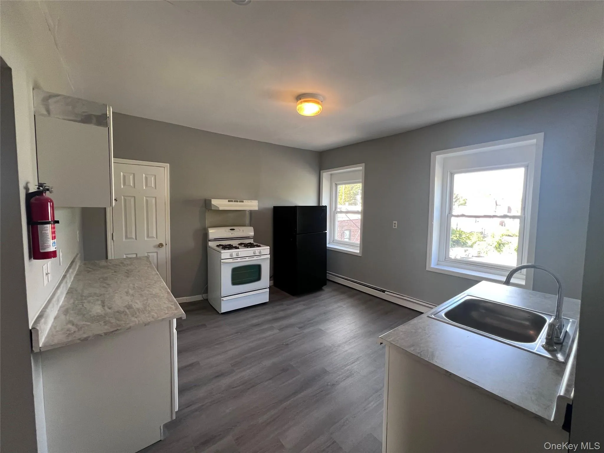 Kitchen with white gas range oven, baseboard heating, dark wood-style flooring, freestanding refrigerator, and light countertops Kitchen with white gas range oven, baseboard heating, dark wood-style flooring, freestanding refrigerator, and light countertops