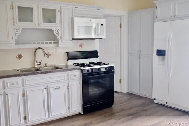 Kitchen featuring white appliances, white cabinetry, light wood-style floors, glass insert cabinets, and backsplash Kitchen featuring white appliances, white cabinetry, light wood-style floors, glass insert cabinets, and backsplash