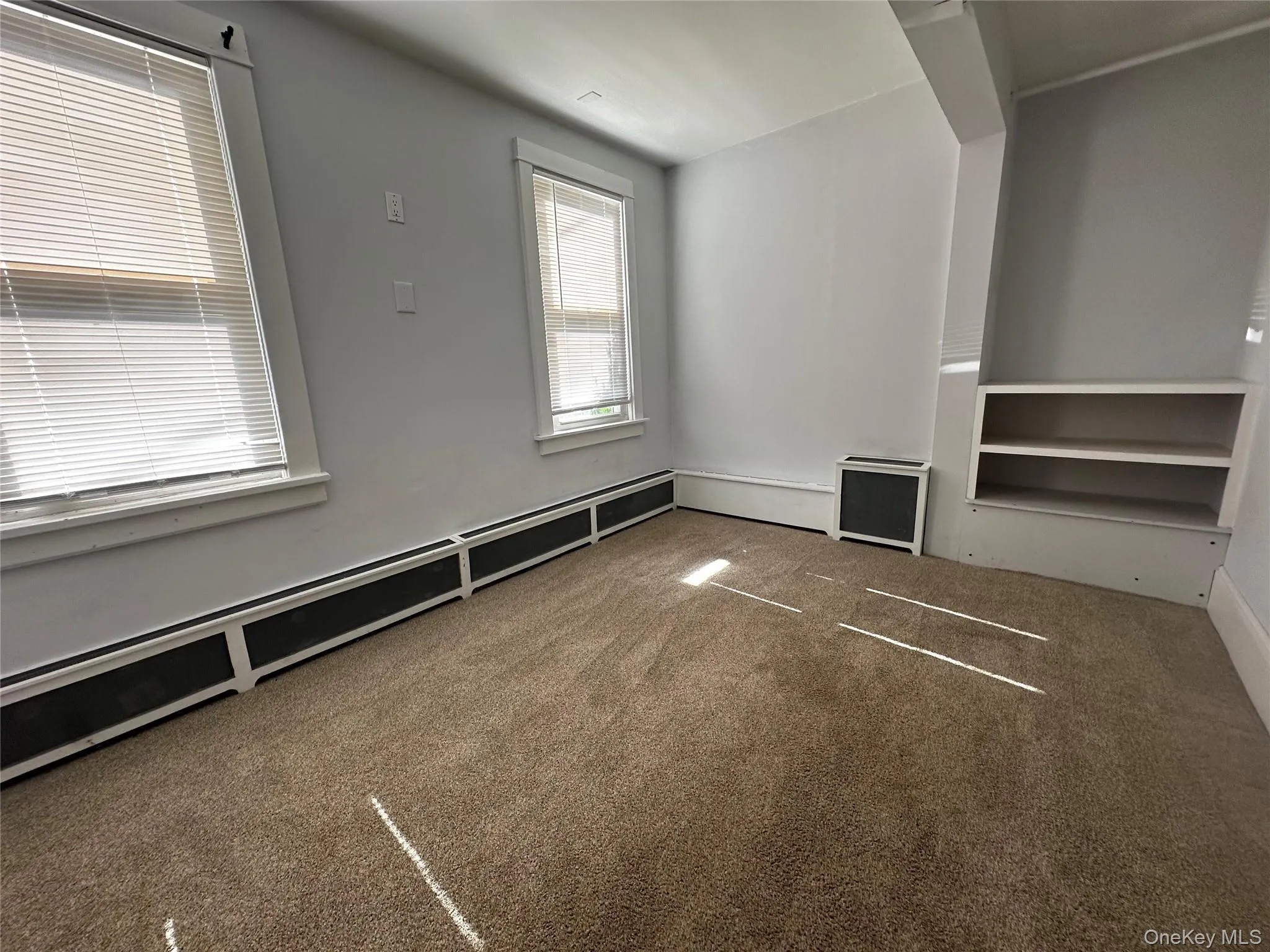 Unfurnished living room featuring carpet and baseboard heating Unfurnished living room featuring carpet and baseboard heating