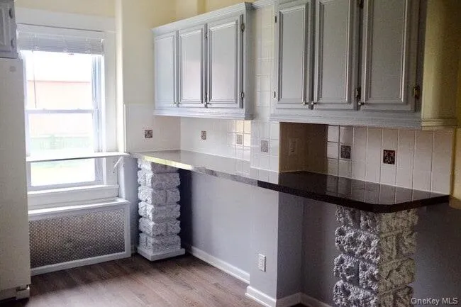 Kitchen featuring radiator heating unit, freestanding refrigerator, light wood finished floors, backsplash, and dark countertops Kitchen featuring radiator heating unit, freestanding refrigerator, light wood finished floors, backsplash, and dark countertops