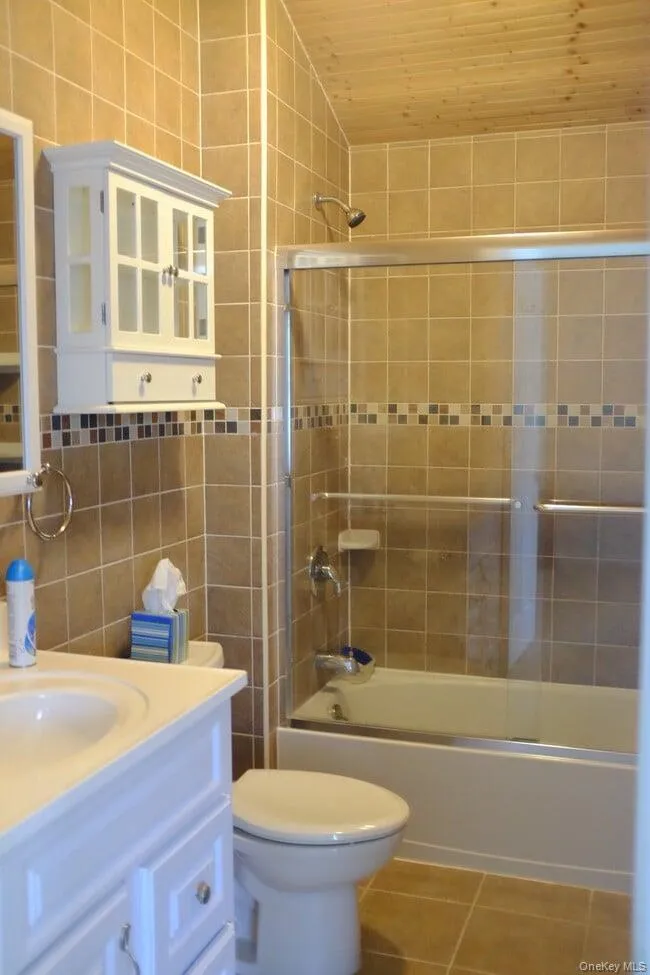 Bathroom with tile walls, shower / bath combination with glass door, vanity, and light tile patterned flooring Bathroom with tile walls, shower / bath combination with glass door, vanity, and light tile patterned flooring