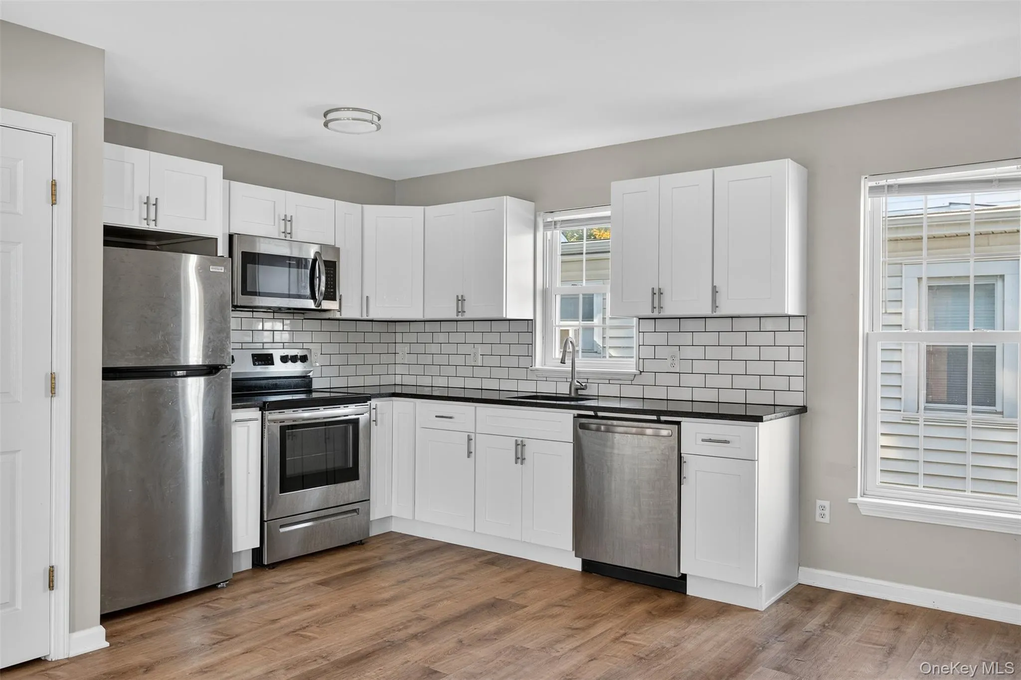 Kitchen with appliances with stainless steel finishes, white cabinetry, light wood-style floors, and dark countertops Kitchen with appliances with stainless steel finishes, white cabinetry, light wood-style floors, and dark countertops