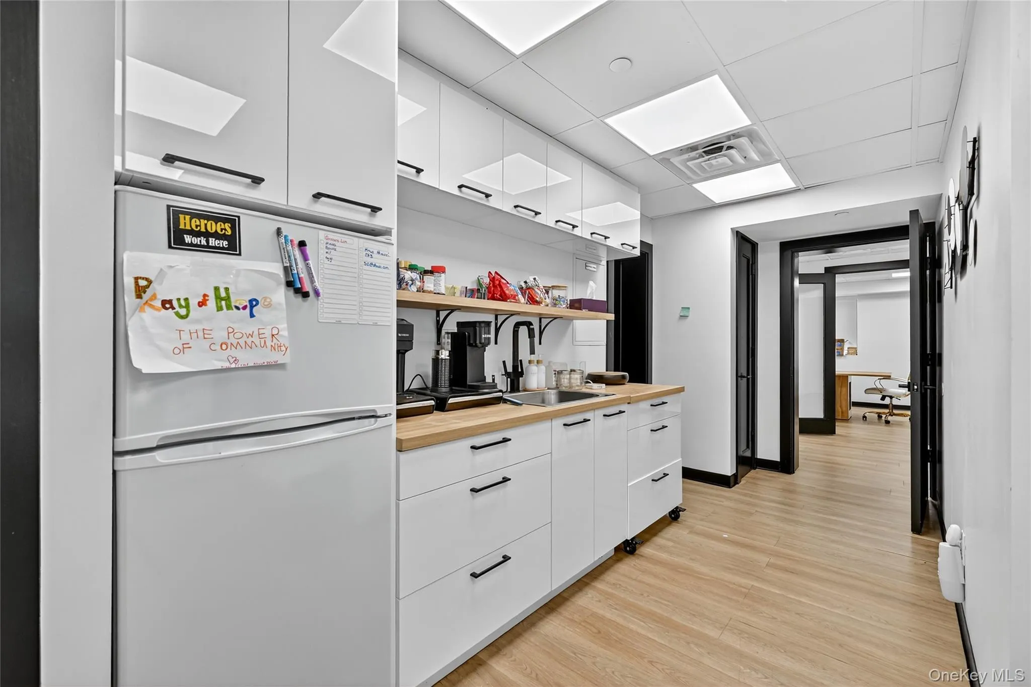Kitchen featuring freestanding refrigerator, white cabinetry, modern cabinets, light wood-style flooring, and a paneled ceiling Kitchen featuring freestanding refrigerator, white cabinetry, modern cabinets, light wood-style flooring, and a paneled ceiling