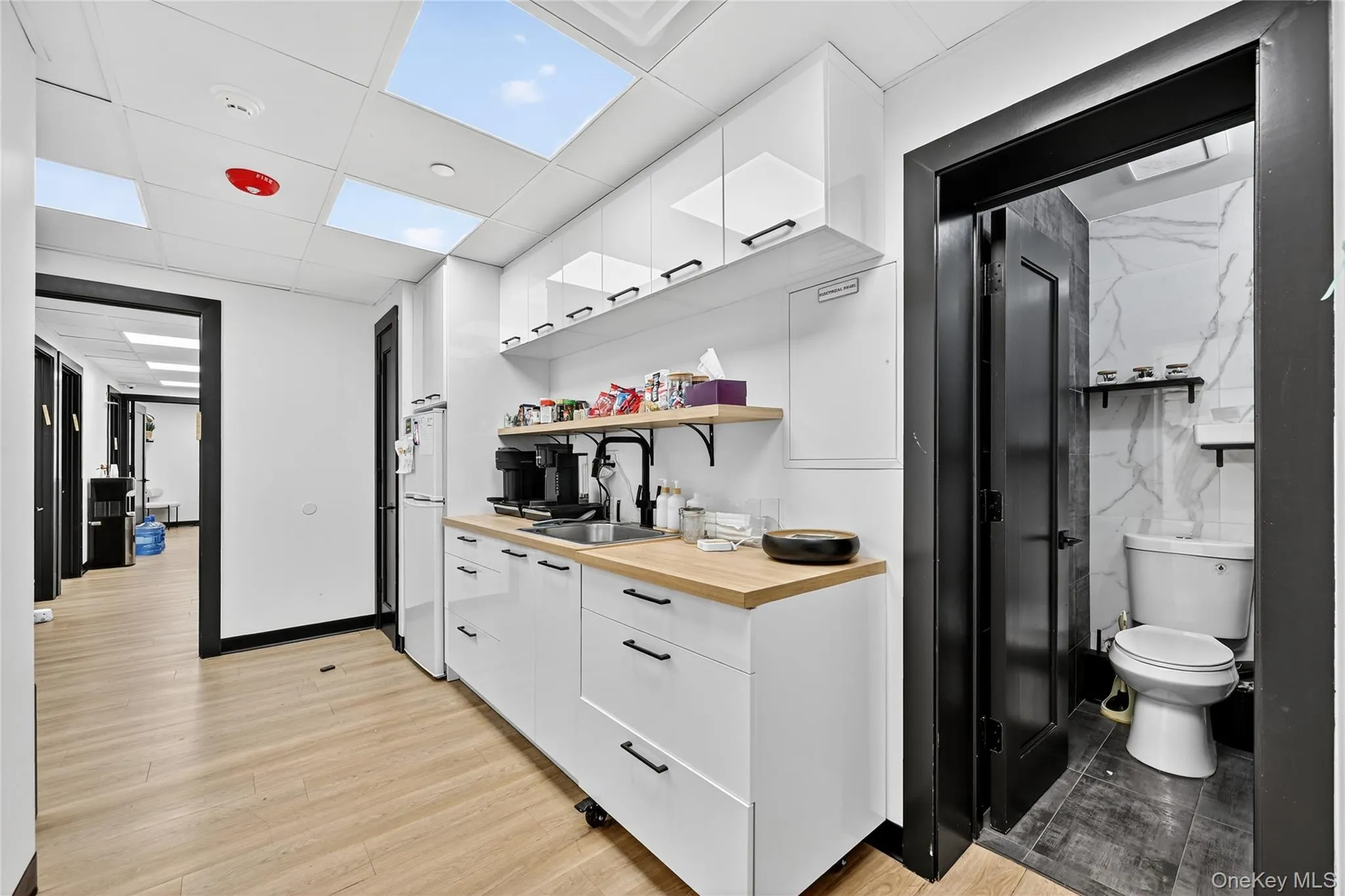 Kitchen featuring white cabinets, open shelves, a drop ceiling, light wood-style flooring, and modern cabinets Kitchen featuring white cabinets, open shelves, a drop ceiling, light wood-style flooring, and modern cabinets