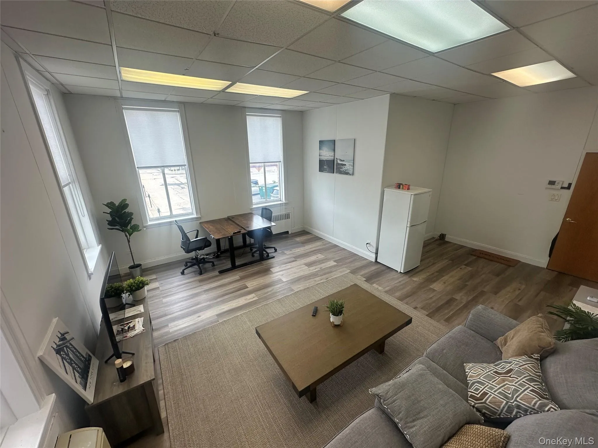 Living area with a paneled ceiling, an office area, wood finished floors, and radiator heating unit Living area with a paneled ceiling, an office area, wood finished floors, and radiator heating unit