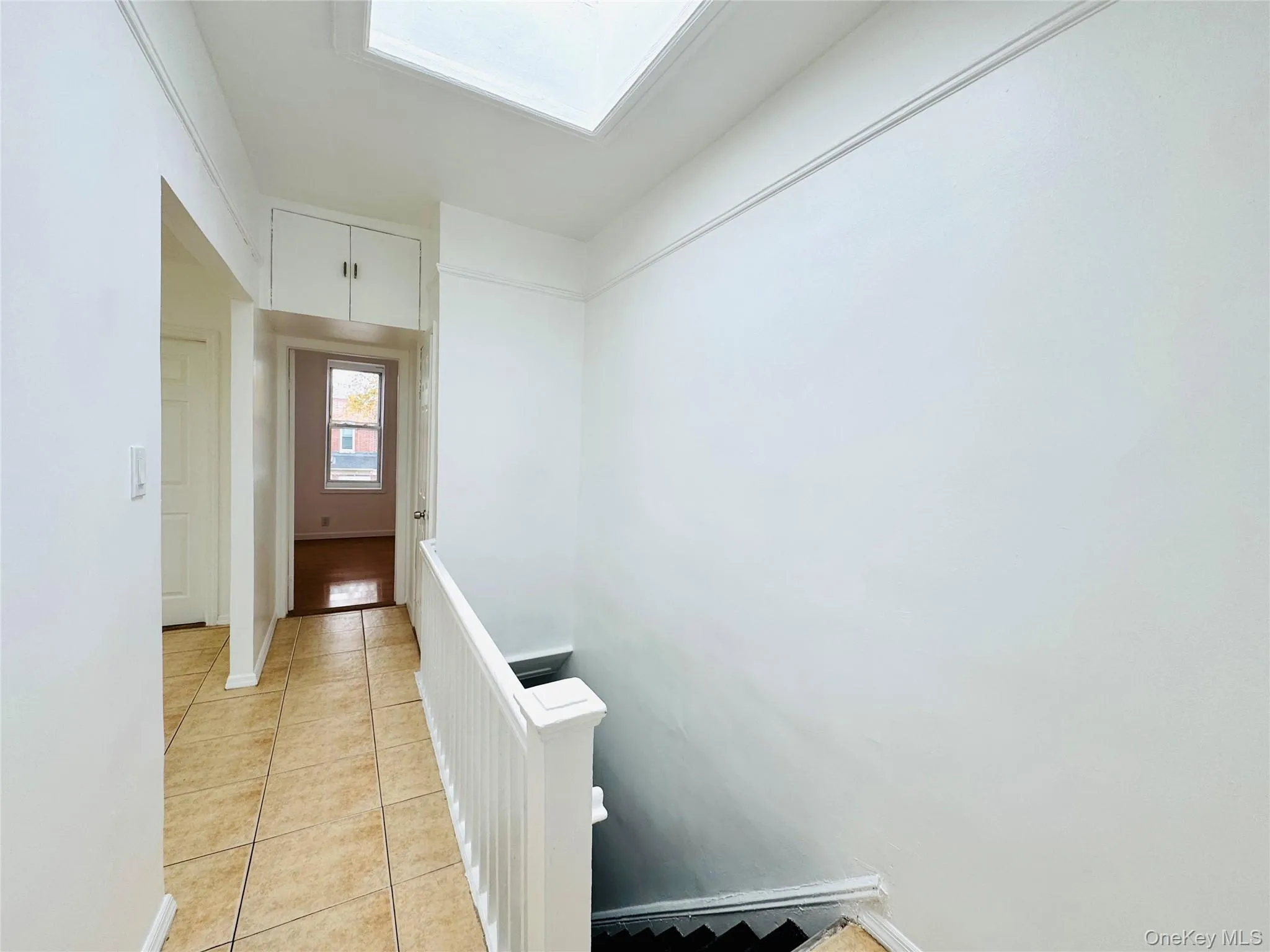 Corridor with light tile patterned floors, a skylight, and an upstairs landing Corridor with light tile patterned floors, a skylight, and an upstairs landing