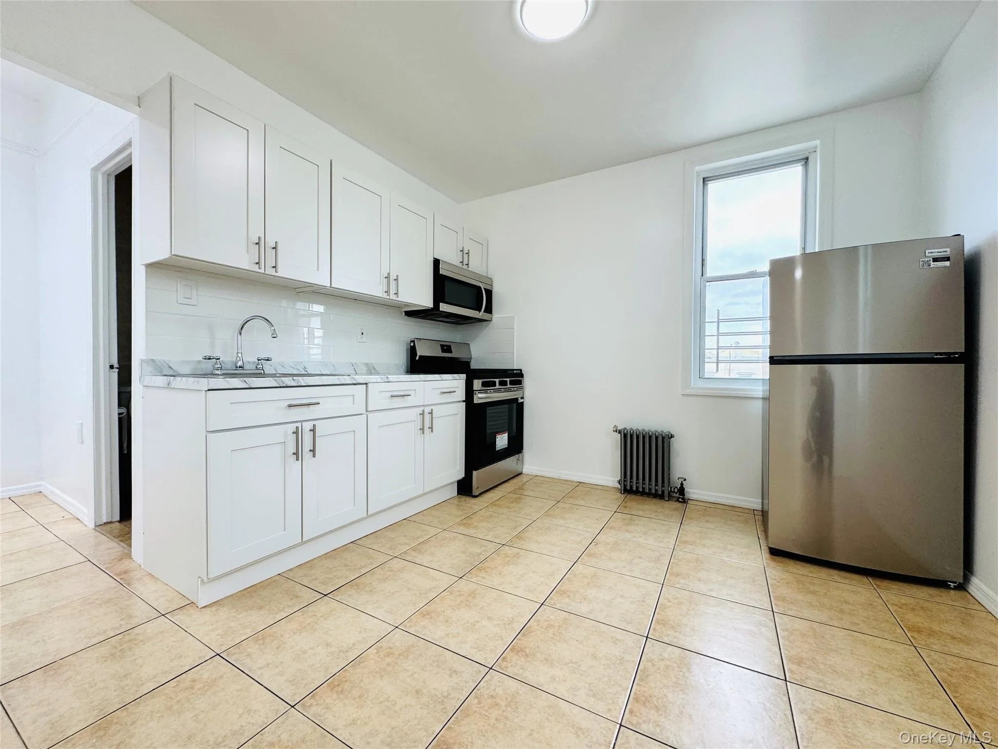 Kitchen with stainless steel appliances, light countertops, white cabinets, tasteful backsplash, and light tile patterned floors Kitchen with stainless steel appliances, light countertops, white cabinets, tasteful backsplash, and light tile patterned floors