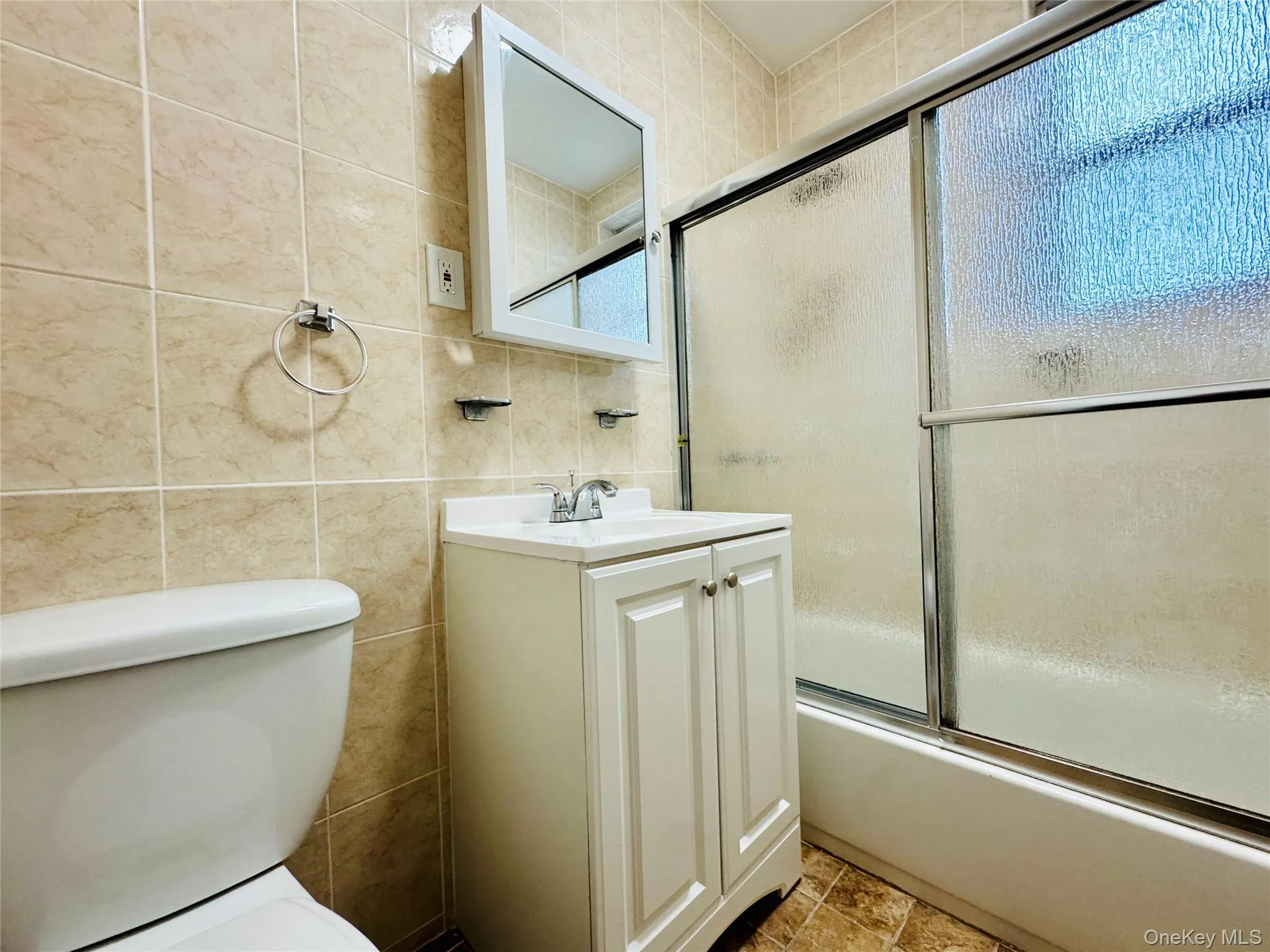 Bathroom with tile walls, vanity, and shower / bath combination with glass door Bathroom with tile walls, vanity, and shower / bath combination with glass door