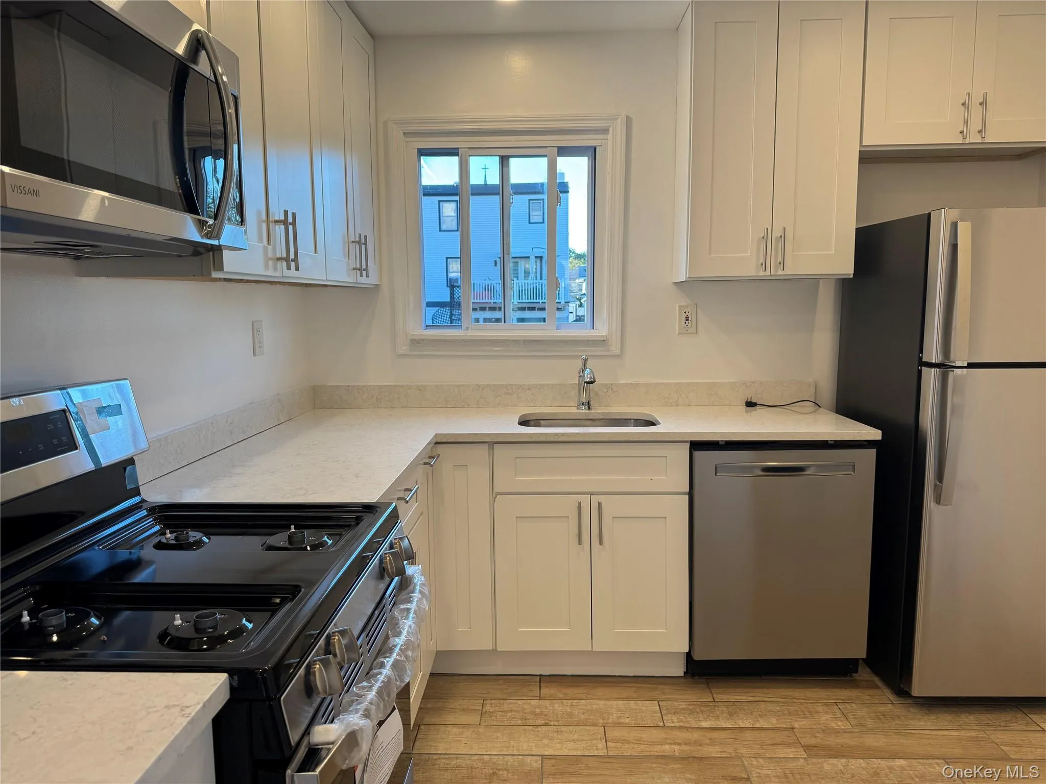 Kitchen featuring stainless steel appliances, white cabinetry, light stone countertops, and wood tiled floors Kitchen featuring stainless steel appliances, white cabinetry, light stone countertops, and wood tiled floors