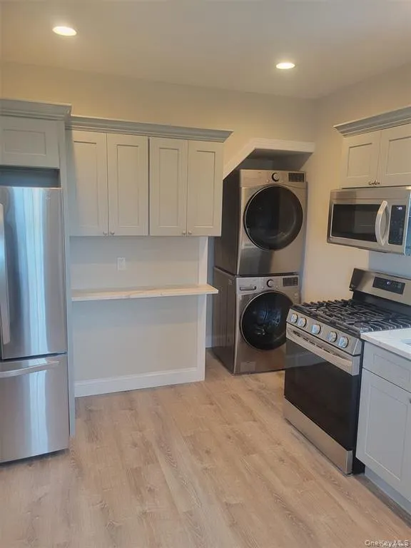 Kitchen with stainless steel appliances, light wood-type flooring, recessed lighting, and stacked washer / dryer Kitchen with stainless steel appliances, light wood-type flooring, recessed lighting, and stacked washer / dryer