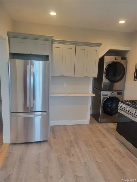 Kitchen with stainless steel appliances, light wood finished floors, stacked washing machine and dryer, recessed lighting, and gray cabinetry Kitchen with stainless steel appliances, light wood finished floors, stacked washing machine and dryer, recessed lighting, and gray cabinetry