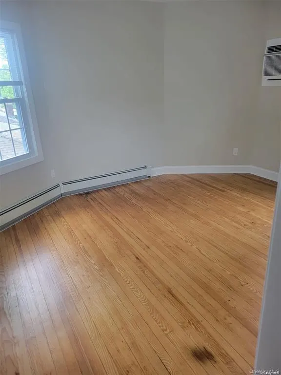 Empty room featuring baseboard heating, light wood-style flooring, and a wall mounted AC Empty room featuring baseboard heating, light wood-style flooring, and a wall mounted AC