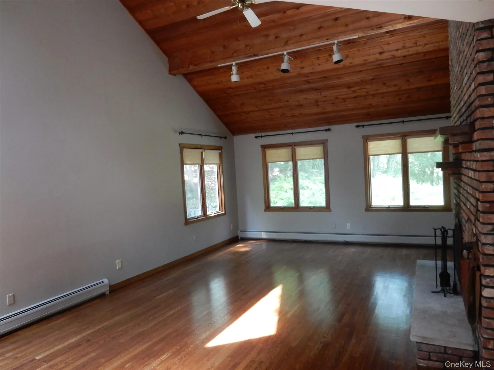 Unfurnished living room featuring rail lighting, dark wood-style flooring, a baseboard radiator, a brick fireplace, and a wood ceiling with exposed beams Unfurnished living room featuring rail lighting, dark wood-style flooring, a baseboard radiator, a brick fireplace, and a wood ceiling with exposed beams