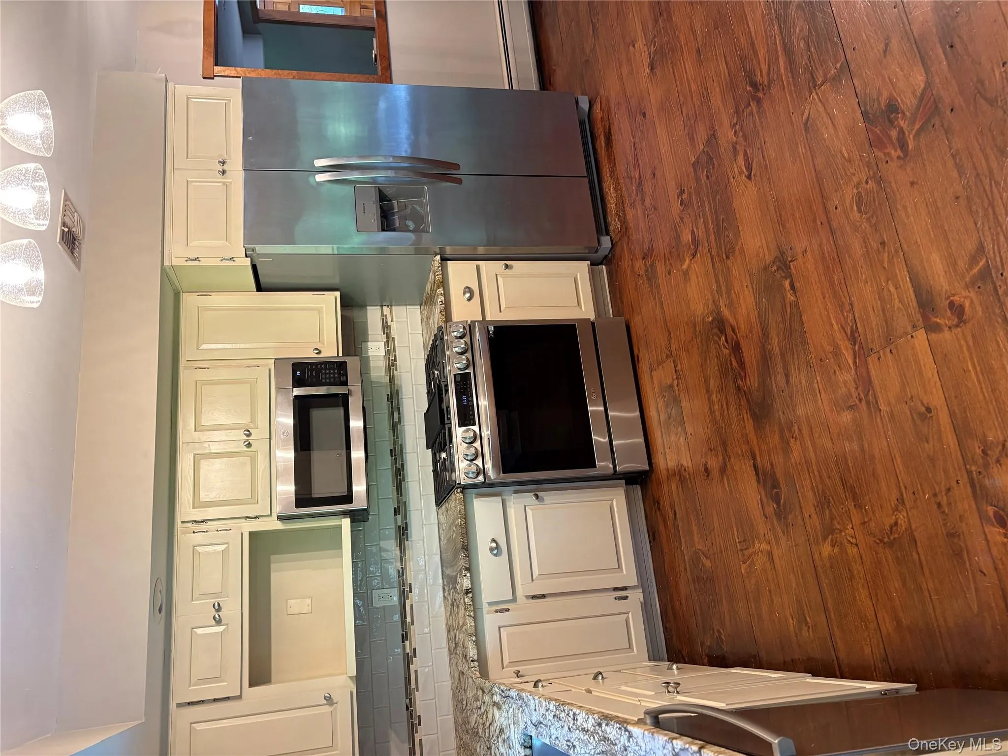 Kitchen featuring stainless steel appliances, light stone counters, backsplash, dark wood-type flooring, and a baseboard heating unit Kitchen featuring stainless steel appliances, light stone counters, backsplash, dark wood-type flooring, and a baseboard heating unit
