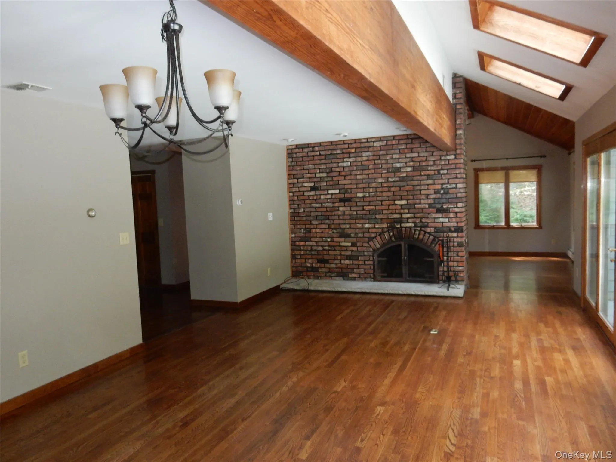 Unfurnished living room featuring a chandelier, dark wood finished floors, and a brick fireplace Unfurnished living room featuring a chandelier, dark wood finished floors, and a brick fireplace