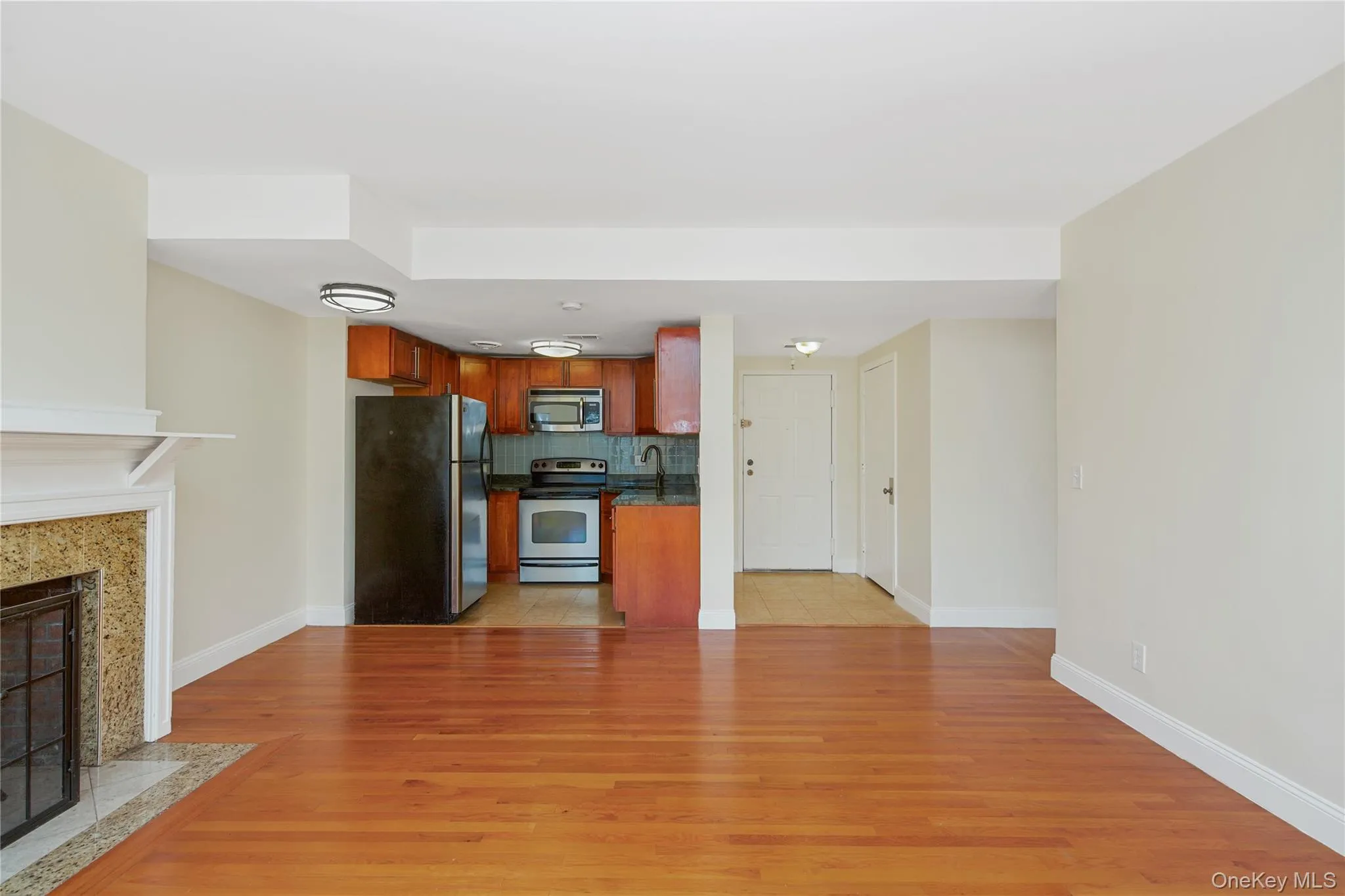 Kitchen featuring open floor plan, decorative backsplash, stainless steel appliances, dark countertops, and light wood-style flooring Kitchen featuring open floor plan, decorative backsplash, stainless steel appliances, dark countertops, and light wood-style flooring